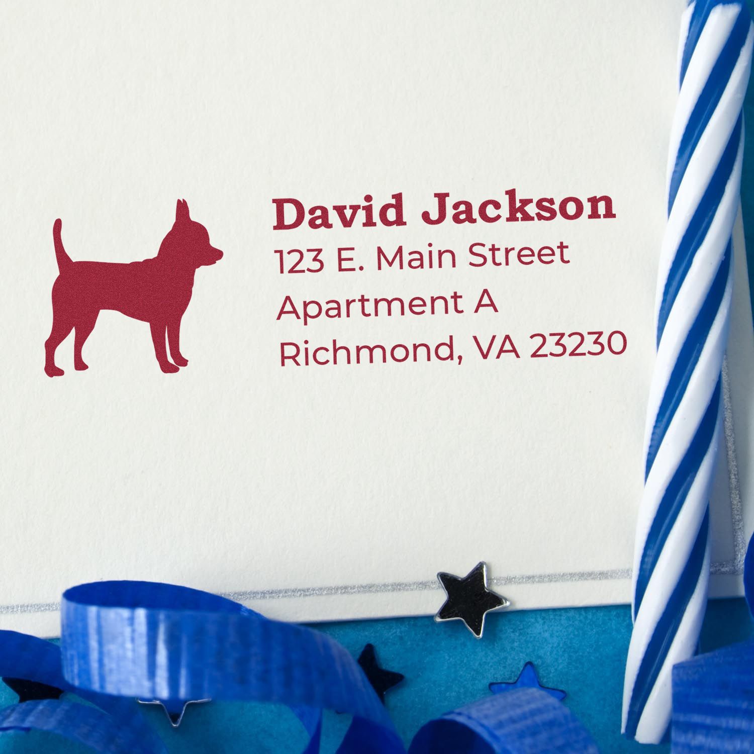 Slim Pre-Inked Chihuahua Address Stamp on an envelope with a red chihuahua silhouette and address. Blue ribbon and star confetti add a festive touch. Perfect for personalized mailings.