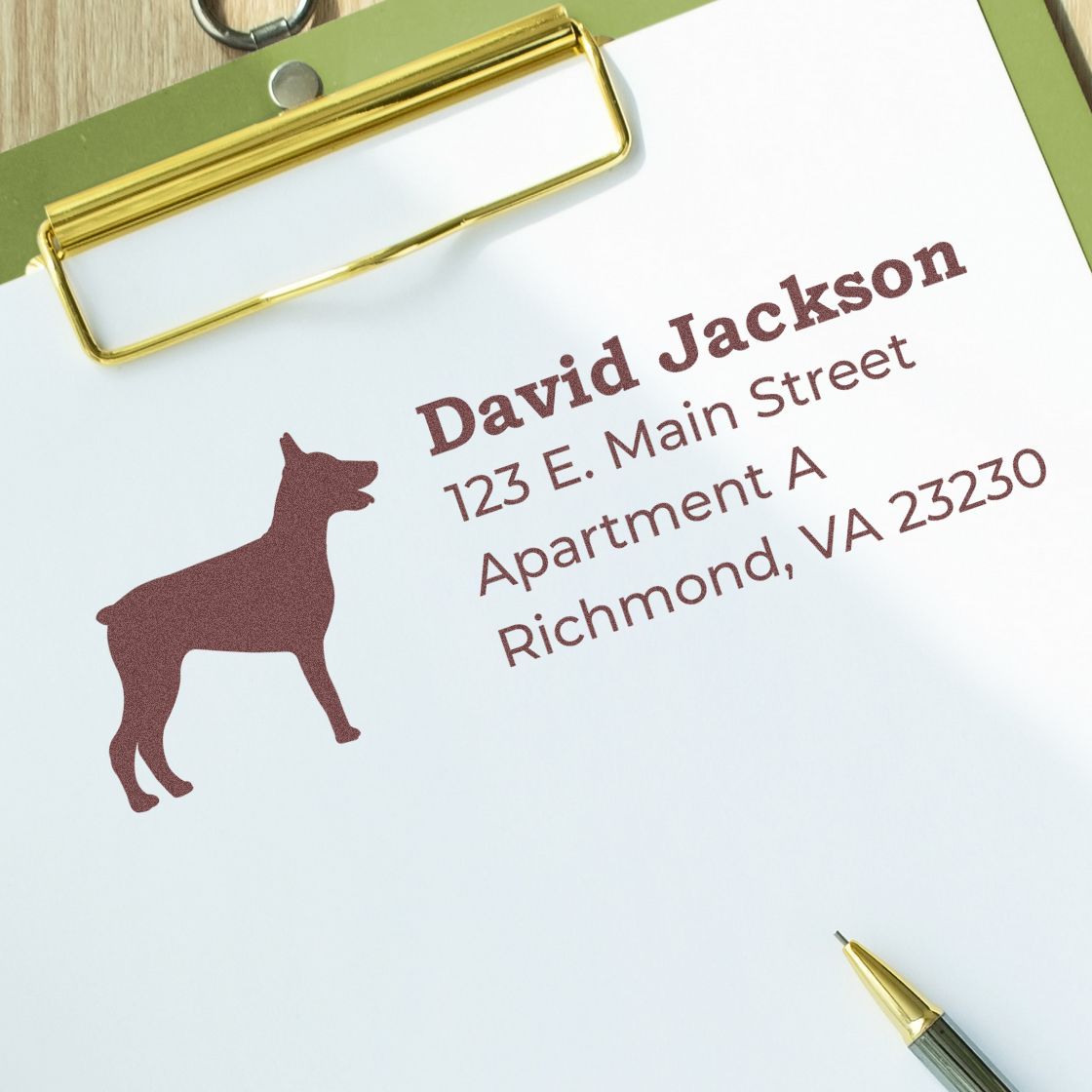 Self-Inking Doberman Dog Address Stamp on paper with a Doberman silhouette and sample address. Clipboard and pen nearby, showcasing the stamp's crisp, professional imprint.