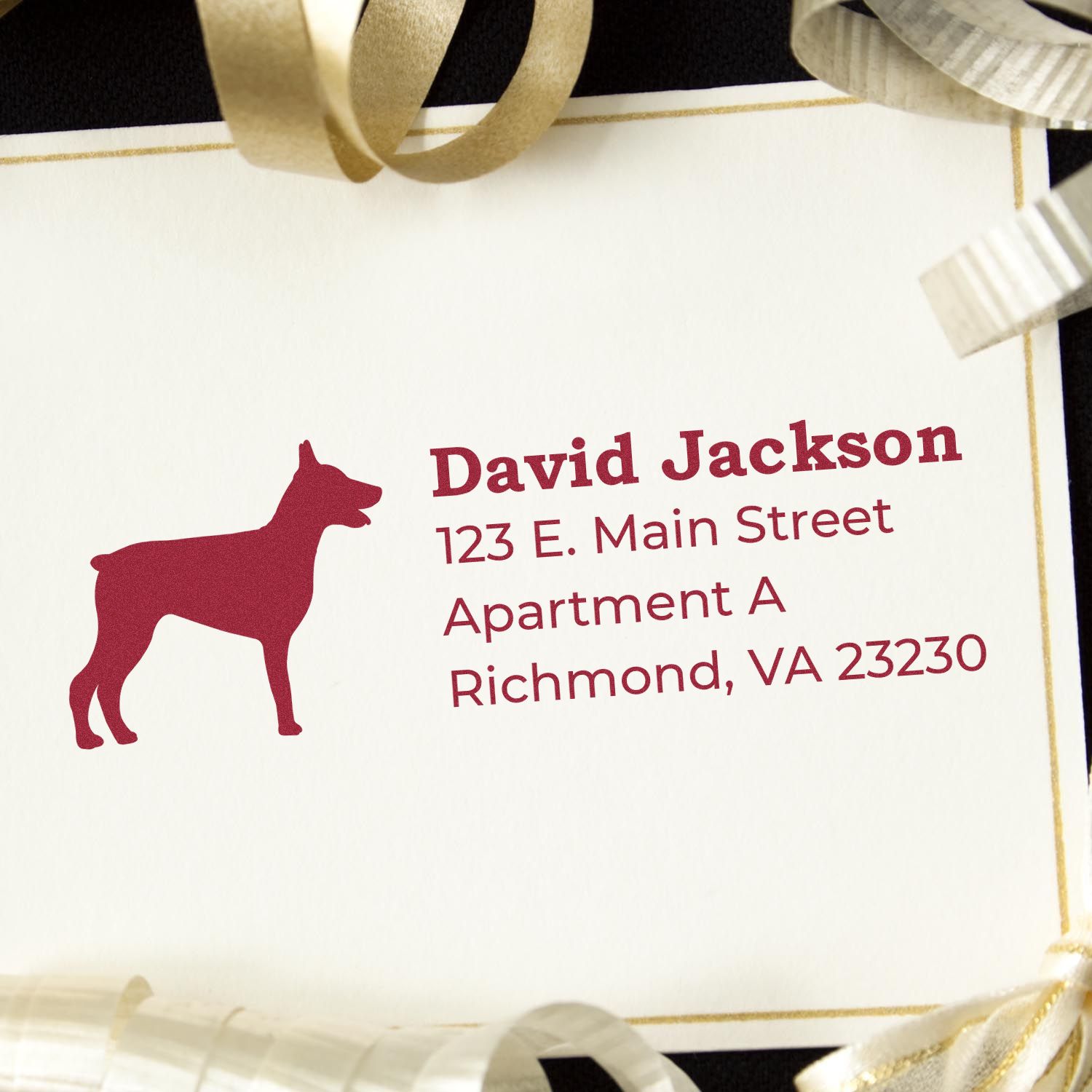 Doberman Silhouette Address Rubber Stamp on a card with red text showing a name and address. The card is surrounded by gold and silver ribbons, highlighting the elegant design of the stamp.