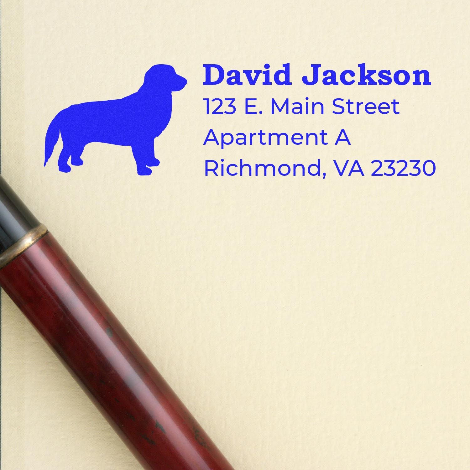 Self-Inking Golden Retriever Dog Address Stamp on paper with a blue dog silhouette and sample address. A pen lies beside the stamped address, showcasing the stamp's crisp, clear impression.