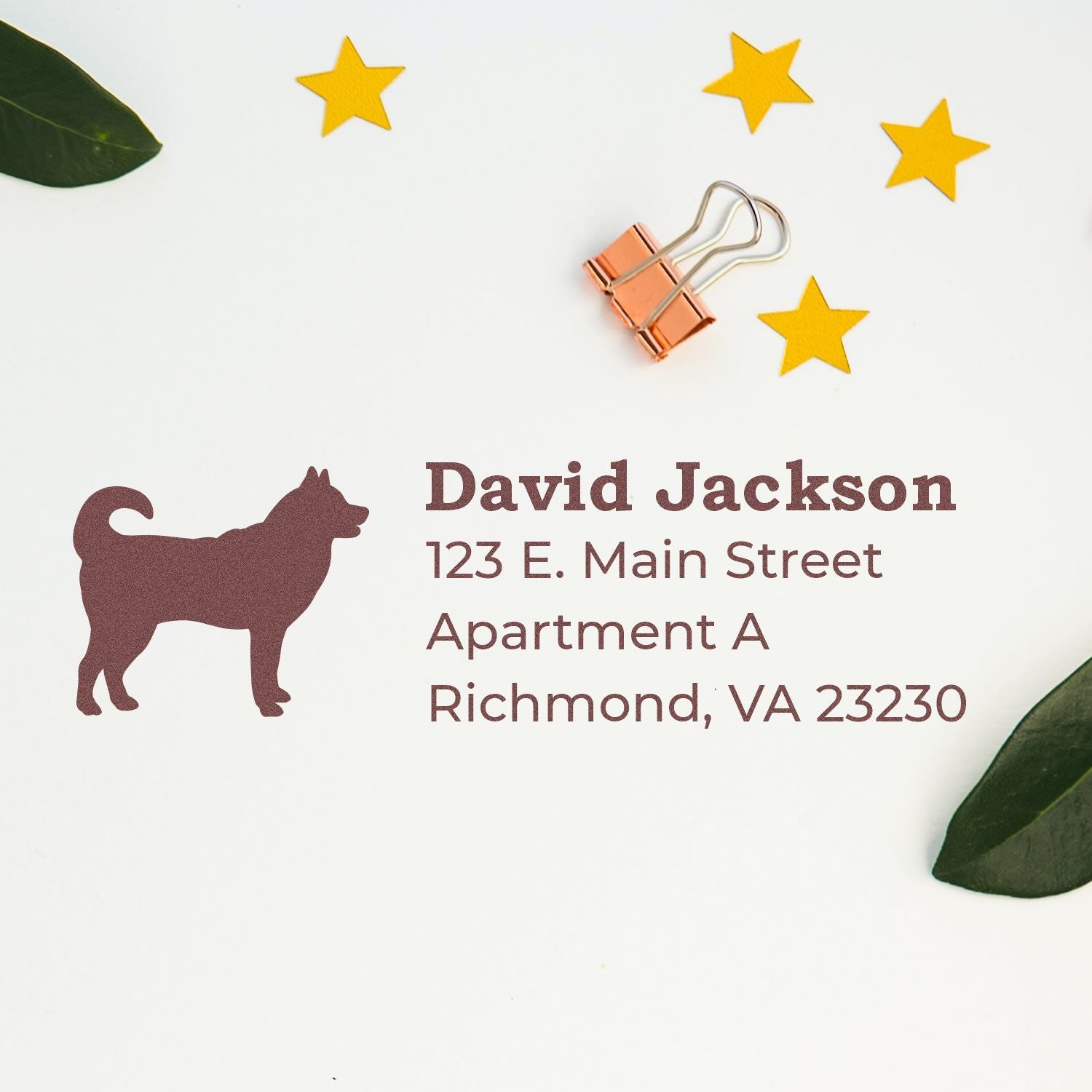 Slim Pre-Inked Husky Address Stamp on white paper with a husky silhouette, sample address, gold stars, and a copper binder clip. Ideal for personalized mailings.