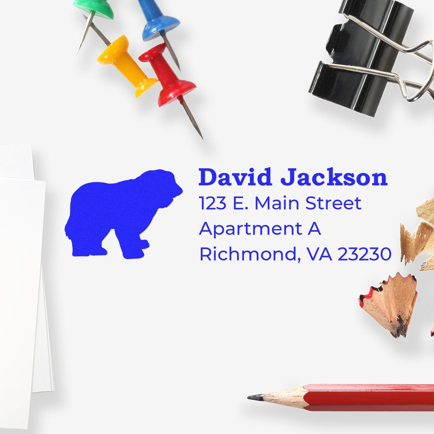 PSI Pre-Inked Personalized Old English Sheepdog Address Stamp on white paper, surrounded by colorful push pins, a binder clip, pencil, and pencil shavings.