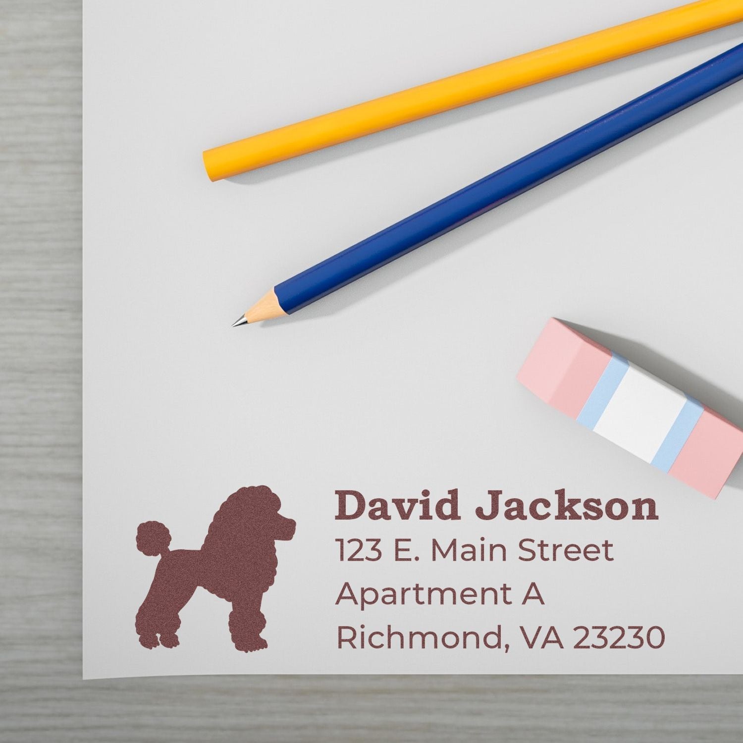 PSI Pre-Inked Personalized Poodle Address Stamp on white paper with a brown poodle silhouette, next to colored pencils and an eraser, displaying an address in Richmond, VA.