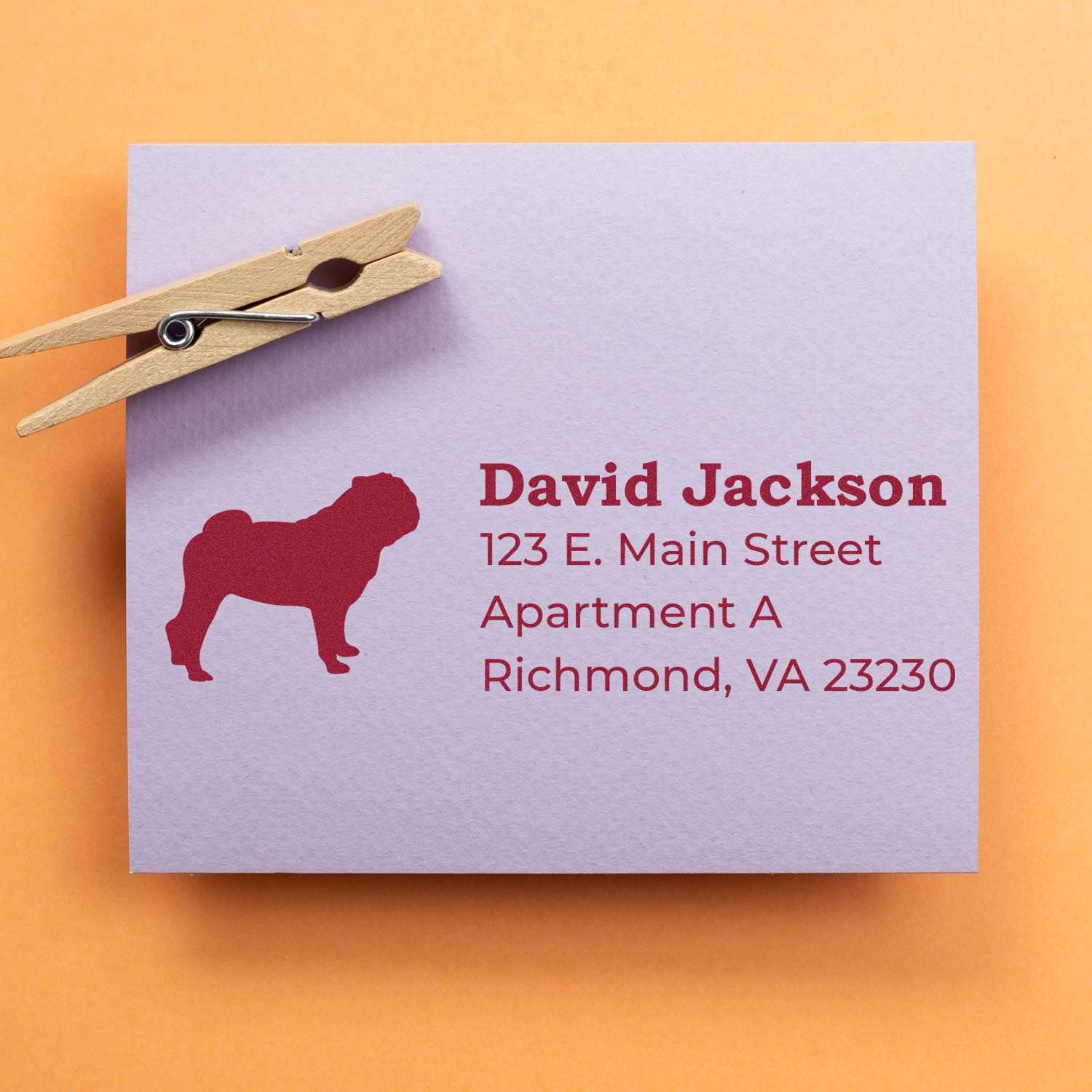 Envelope with a red pug silhouette and address stamped using the Self-Inking Pug Dog Address Stamp, clipped with a wooden clothespin on an orange background.