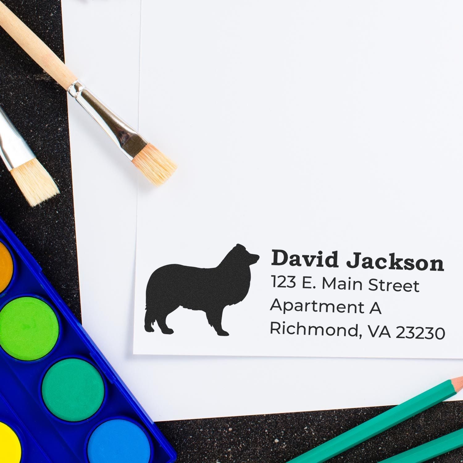 Self-Inking Shetland Sheepdog Dog Address Stamp on white paper with colorful paints and brushes nearby, showcasing a silhouette of the dog and sample address text.