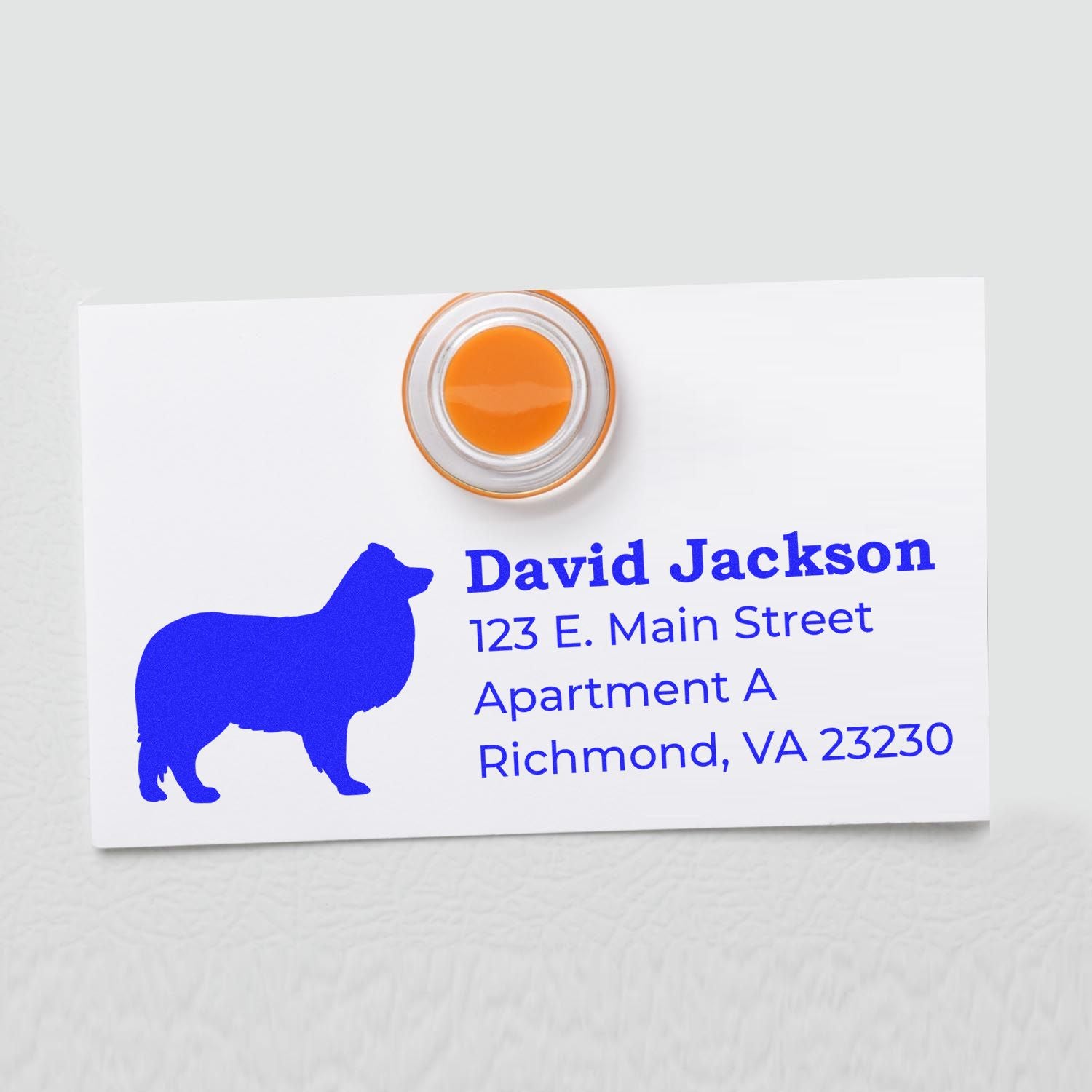 Self-Inking Shetland Sheepdog Dog Address Stamp on a white card with blue text and a silhouette of a Shetland Sheepdog. The stamp is orange and round, showcasing a personalized address.