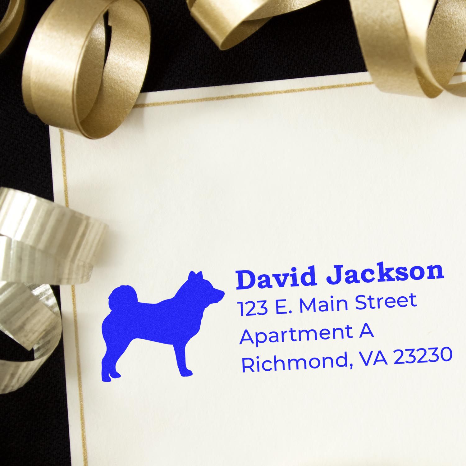 Self-Inking Shiba Inu Dog Address Stamp on a white envelope with blue ink, featuring a Shiba Inu silhouette. Surrounded by gold and silver ribbon, creating a festive and elegant presentation.