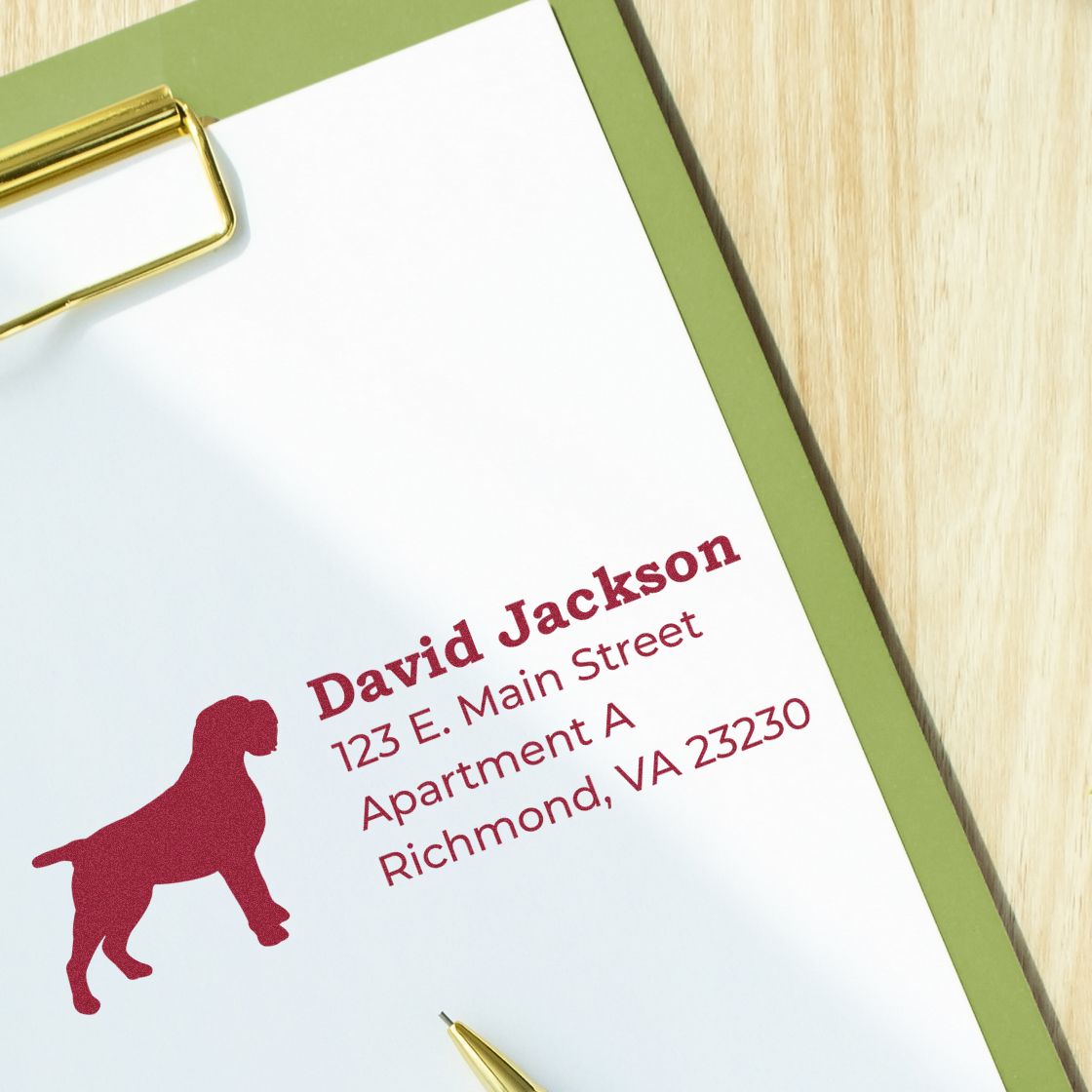 Self-Inking Wirehaired Pointing Griffon Dog Address Stamp on paper with a red dog silhouette, displaying an address in bold text. Clipboard and pen are visible on a wooden surface.