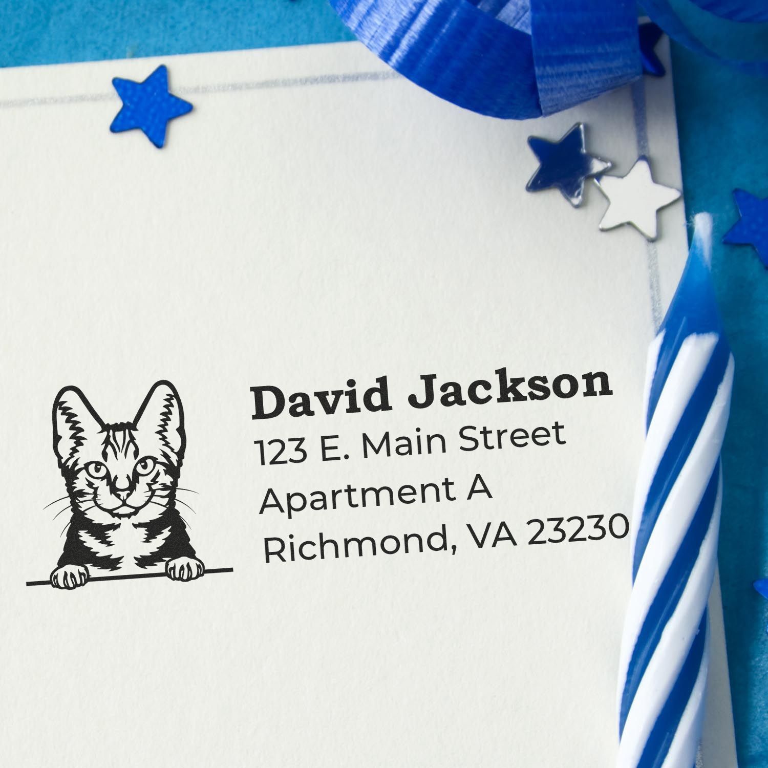 Self-Inking American Shorthair Custom Address Stamp on an envelope with a cat design, surrounded by blue decorations and a striped candle.