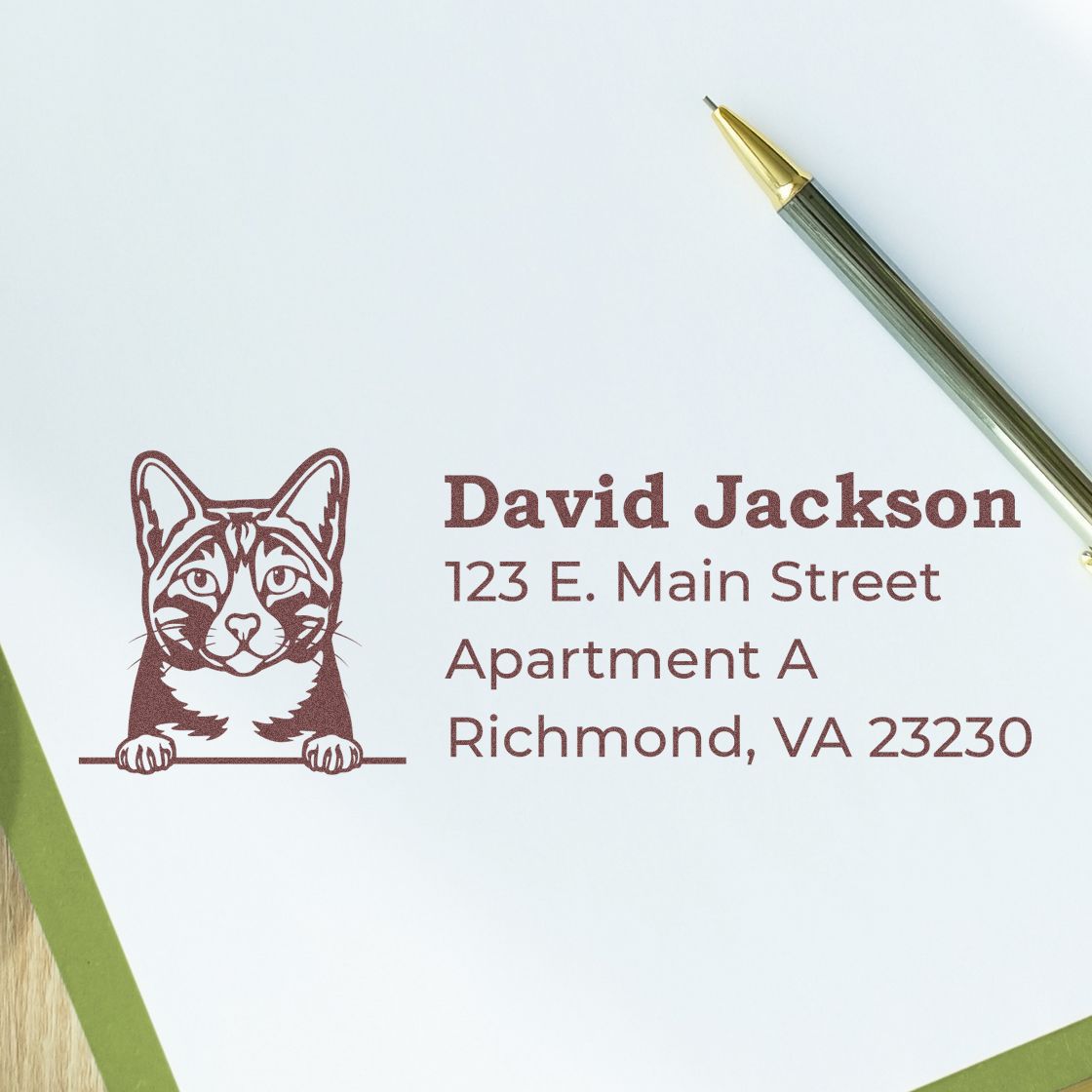 Self-Inking Arabian Mau Custom Address Stamp on white paper with a cat design, showing an address. A pen lies nearby, emphasizing the stamp's use for personalizing correspondence.