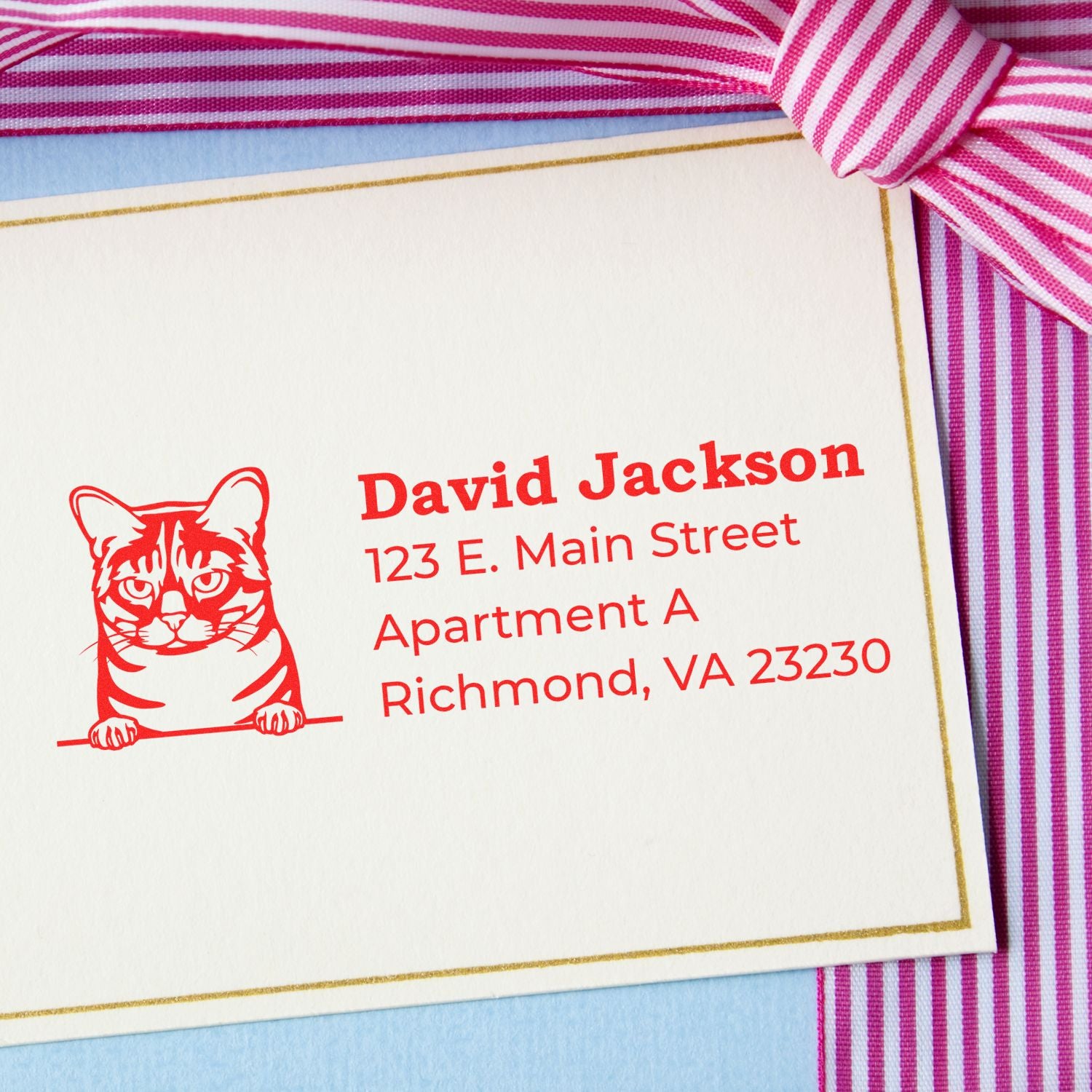 Wood Handle Australian Mist Cat Address Stamp on an envelope with a red cat design and address in bold red text, placed on a blue surface with a pink striped ribbon.