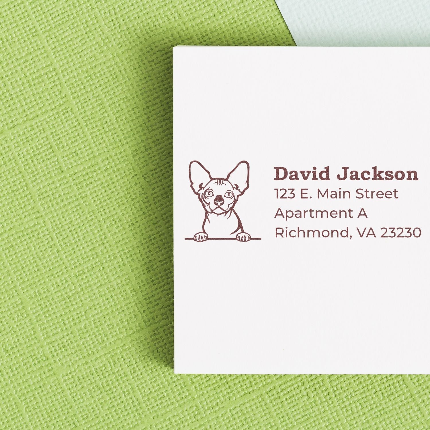 Self-Inking Bambino Custom Address Stamp featuring a cute dog design, shown on a white envelope against a green textured background.