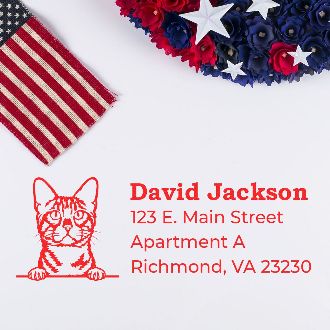 Self-Inking Bengal Custom Address Stamp with a red cat design, displaying an address. Background includes a partial American flag and a patriotic floral arrangement.