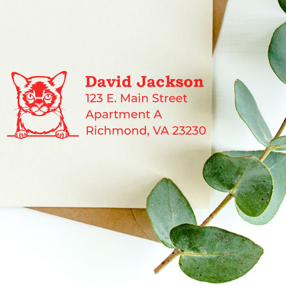 Wood Handle Burmese Cat Address Stamp on an envelope with a red cat design and address details. Eucalyptus leaves are placed beside the envelope, creating a stylish and personalized look.