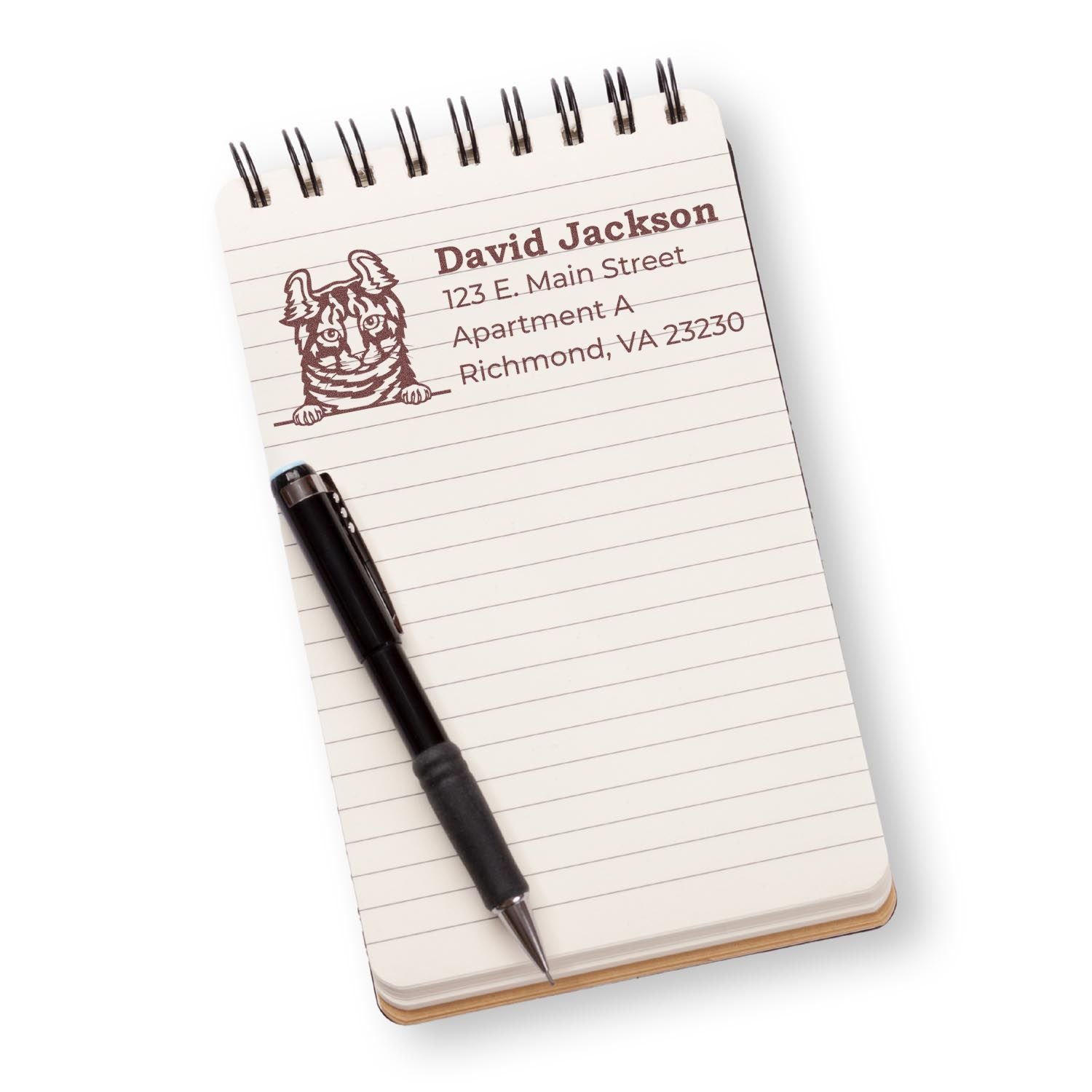 A notepad with a pen displays an impression from the Slim Pre-Inked Highlander Peeking Cat Return Address Stamp, featuring a cat illustration and sample address text in brown ink.