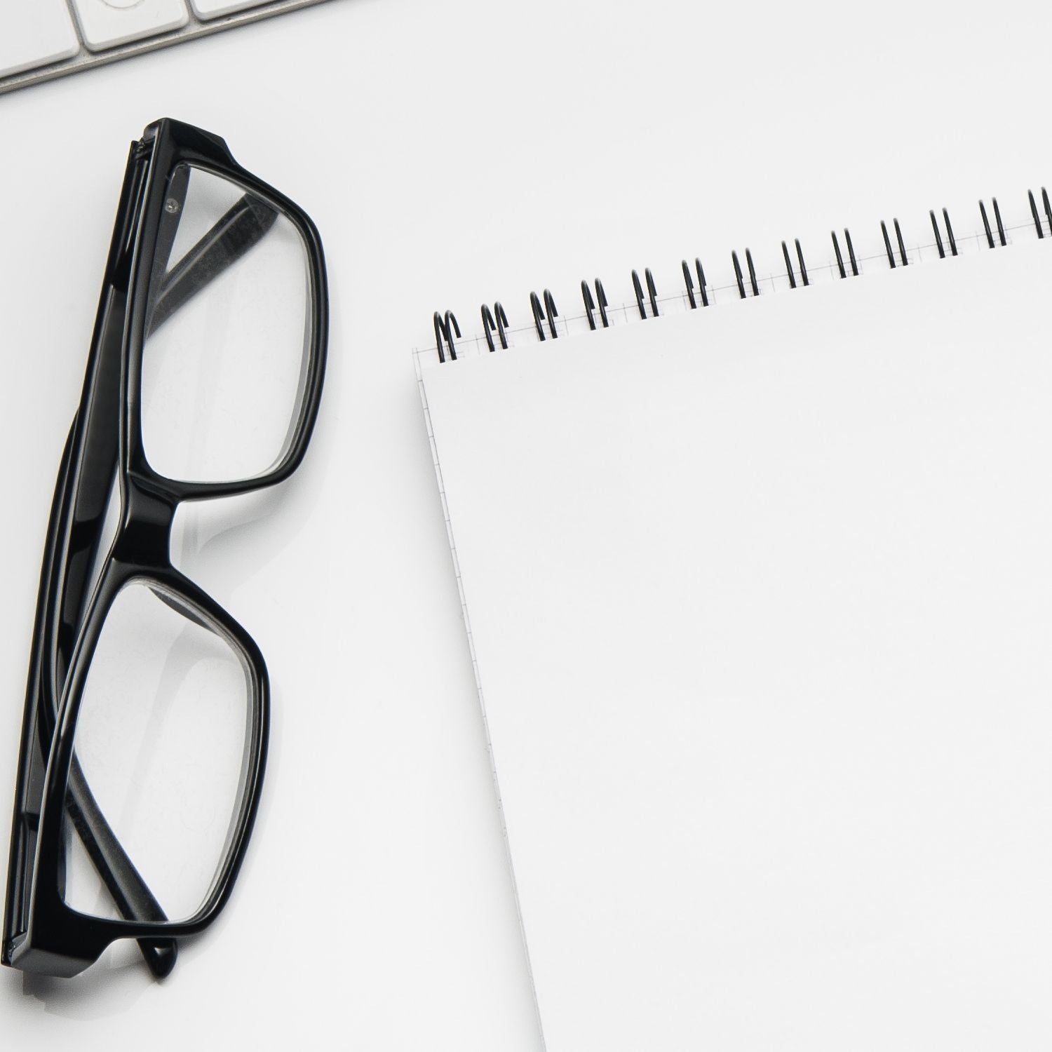 A pair of black glasses rests on a white desk beside a spiral notebook. The Self-Inking Himalayan Custom Address Stamp is partially visible, showcasing its sleek design and functionality.