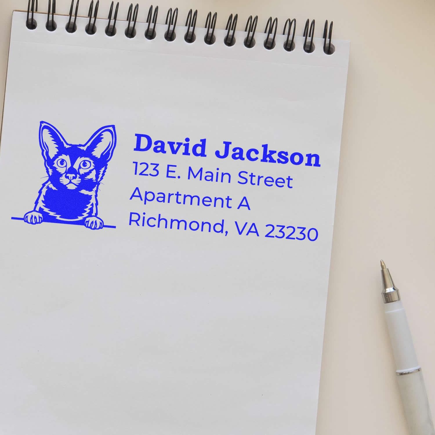 PSI Pre-Inked Peeking Javanese Cat Personalized Address Stamp on notepad, featuring a blue cat illustration and sample address. Pen nearby, showcasing elegant and practical design.