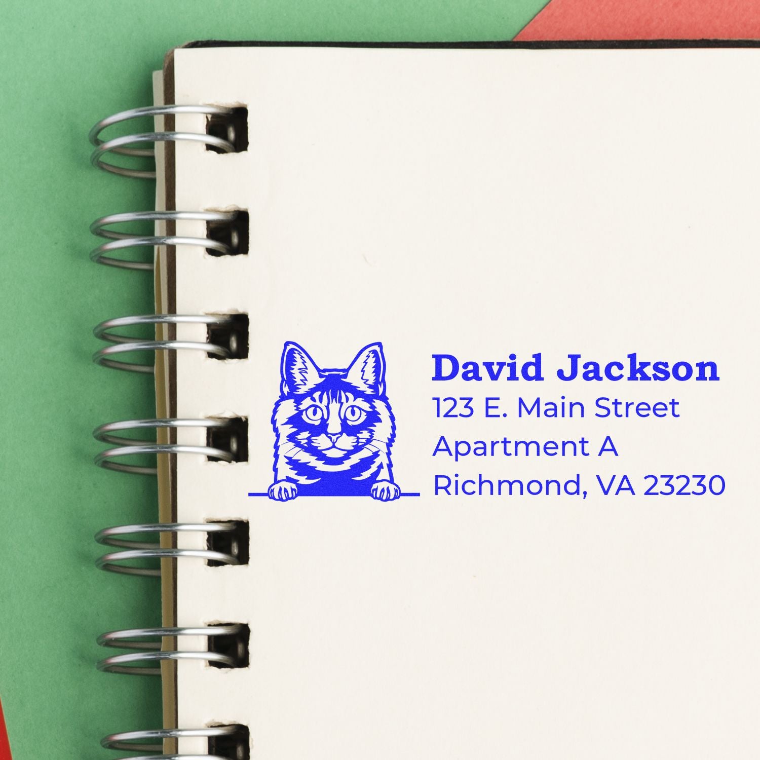 A blue Self-Inking Kurilian Bobtail Custom Address Stamp imprint on a notebook page, featuring a cat illustration and sample address details in bold text.