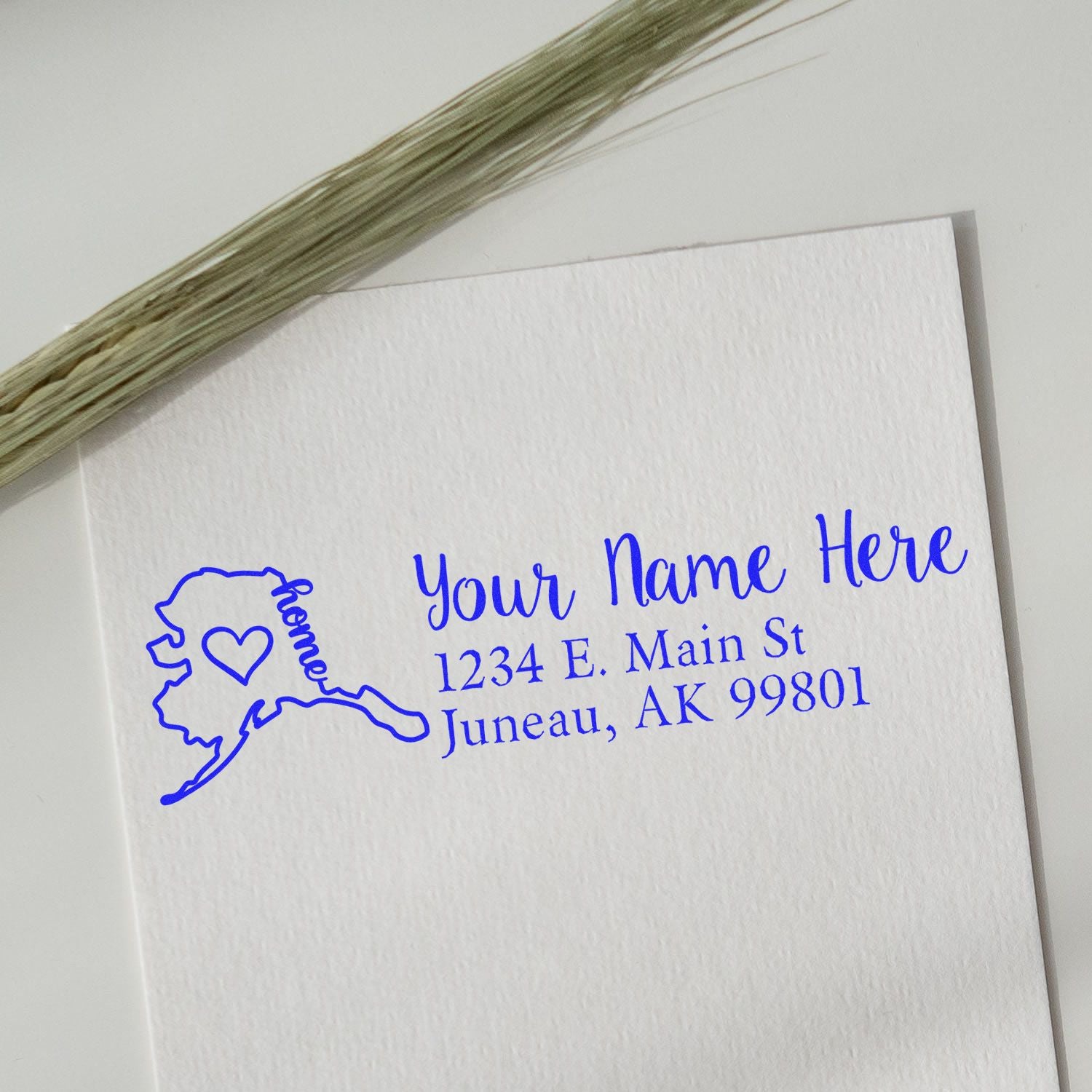 Wood Handle Alaska Custom Address Rubber Stamp on white paper with blue ink, featuring a map of Alaska and personalized address. Decorative grass in the background.