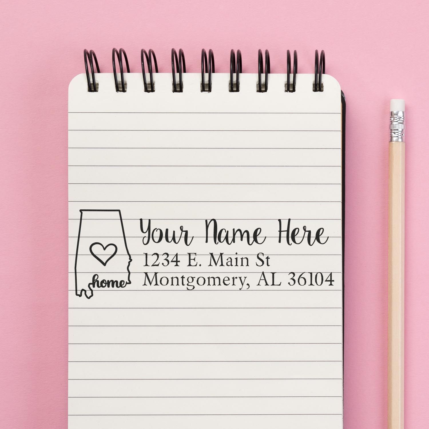 Alabama Self-Inking State Love Address Stamp on a notepad with a pink background and pencil, featuring a heart design and customizable address fields.