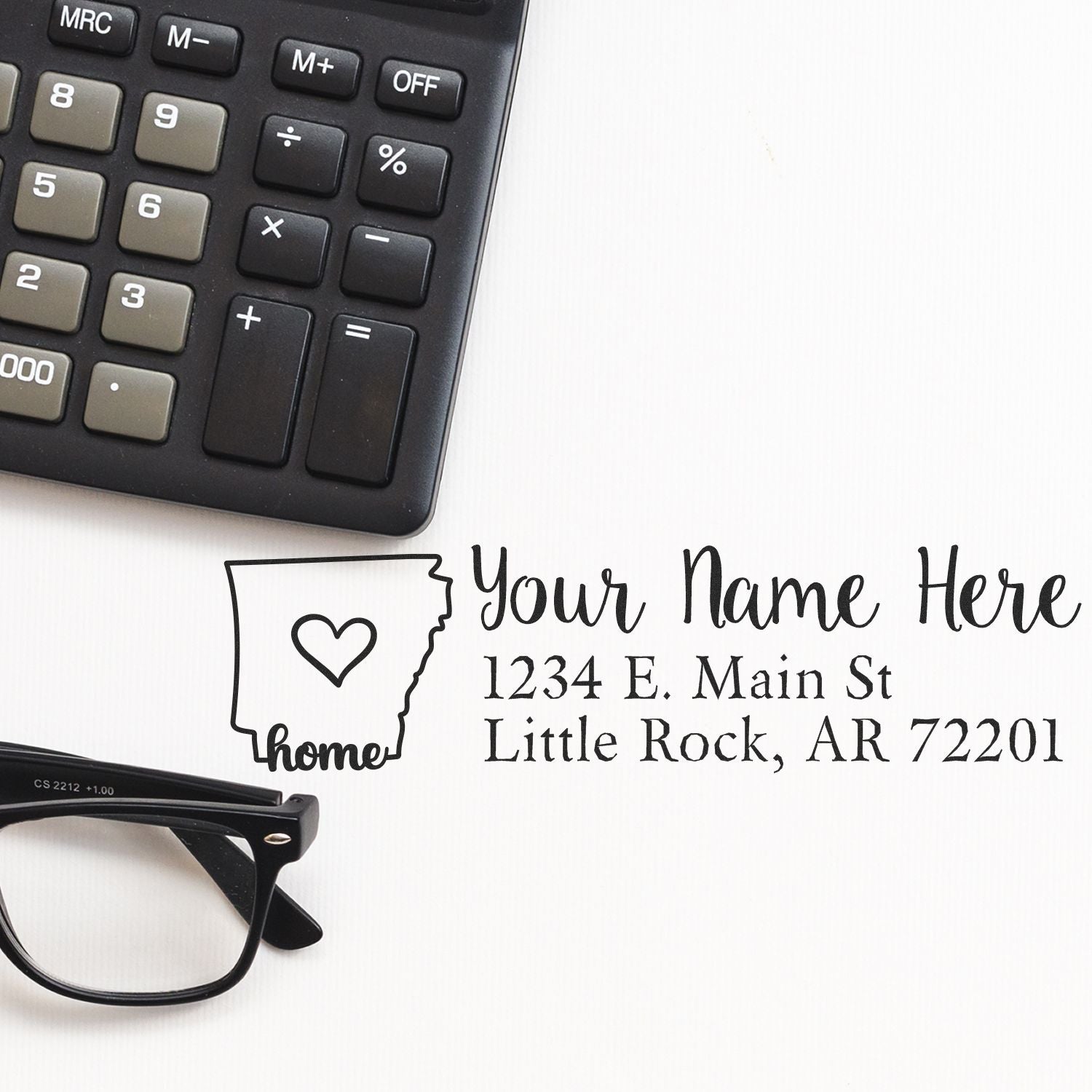 PSI Pre-Inked Personalized Arkansas State Love Address Stamp next to a calculator and glasses, featuring a heart design and customizable address text for Little Rock, AR.