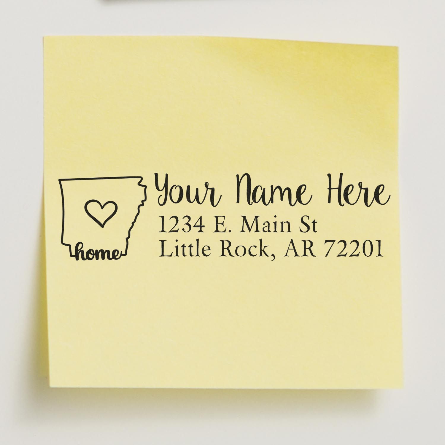 Yellow sticky note with a PSI Pre-Inked Personalized Arkansas State Love Address Stamp design, featuring a heart inside the state outline and customizable address text in elegant black font.