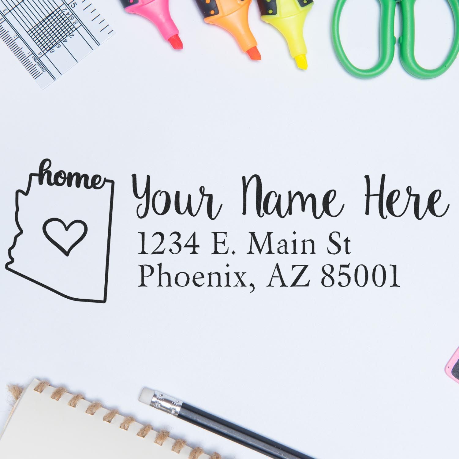 Arizona Self-Inking State Love Address Stamp on paper with 'Your Name Here' and Phoenix address, surrounded by colorful office supplies like highlighters, scissors, and a ruler.