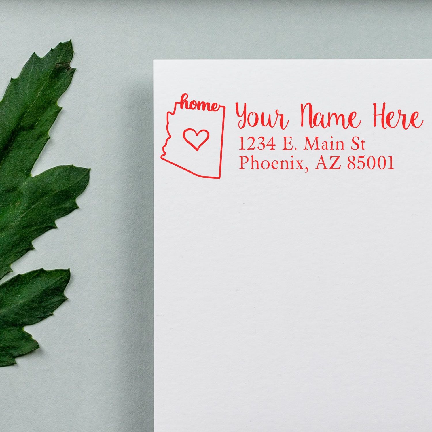 Arizona Self-Inking State Love Address Stamp on white paper with a red outline of Arizona and heart, next to a green leaf. Text reads Your Name Here, 1234 E. Main St, Phoenix, AZ 85001.