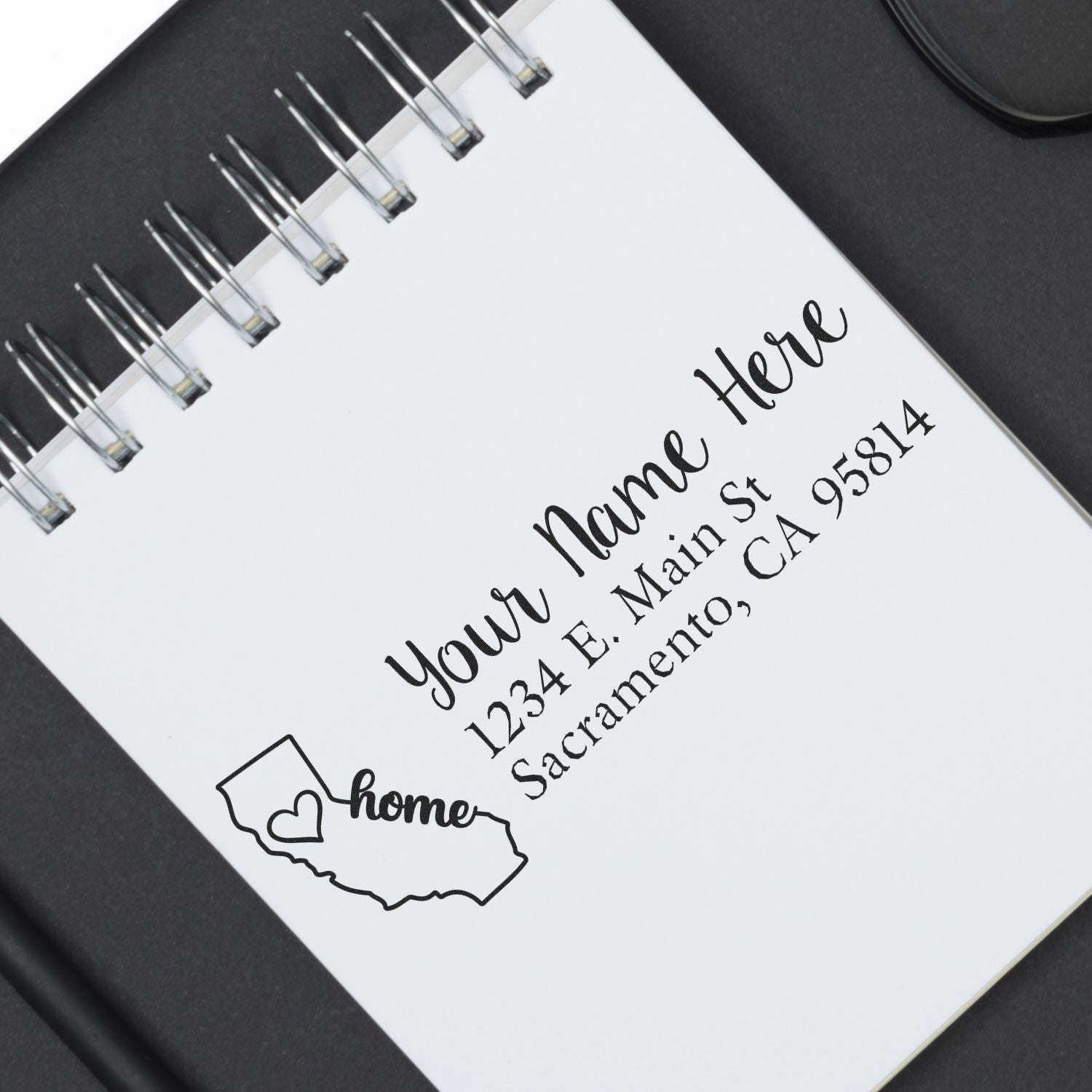 PSI Pre-Inked Personalized California State Love Address Stamp on a notepad, featuring a heart and home text within the state outline, displaying a sample address in elegant black ink.