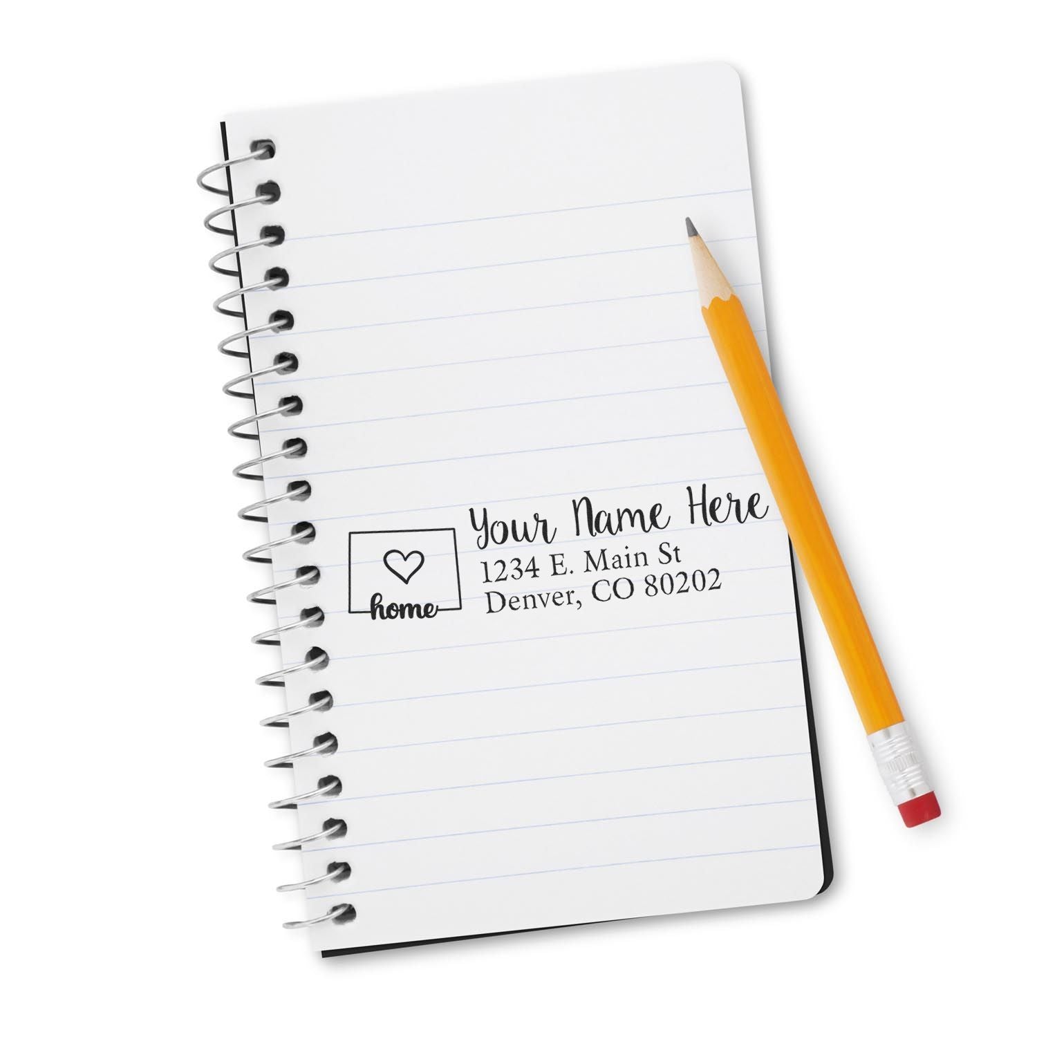 A spiral notebook with a stamped address using the Wood Handle Colorado Custom Address Rubber Stamp. The stamp shows a heart icon, name, and address in Denver, CO. A yellow pencil lies beside it.