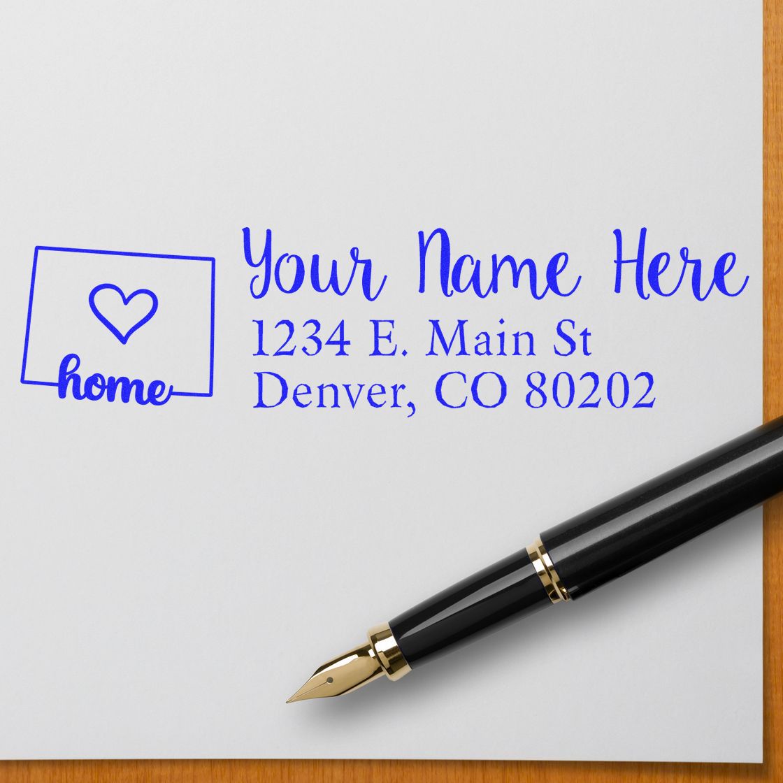 PSI Pre-Inked Personalized Colorado State Love Address Stamp on white paper with a fountain pen, featuring a heart and home design, and customizable address in blue ink.