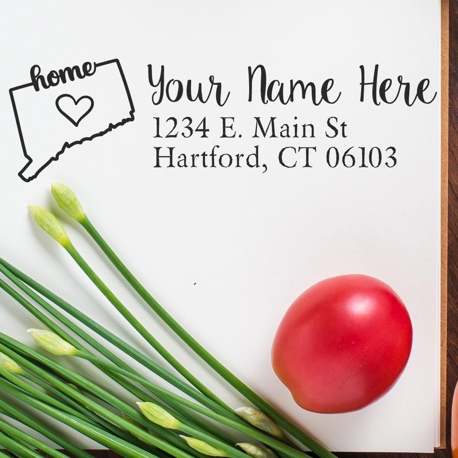 Wood Handle Connecticut Custom Address Rubber Stamp on paper with a heart design, next to green onions and a red tomato, showcasing personalized address details in elegant script.