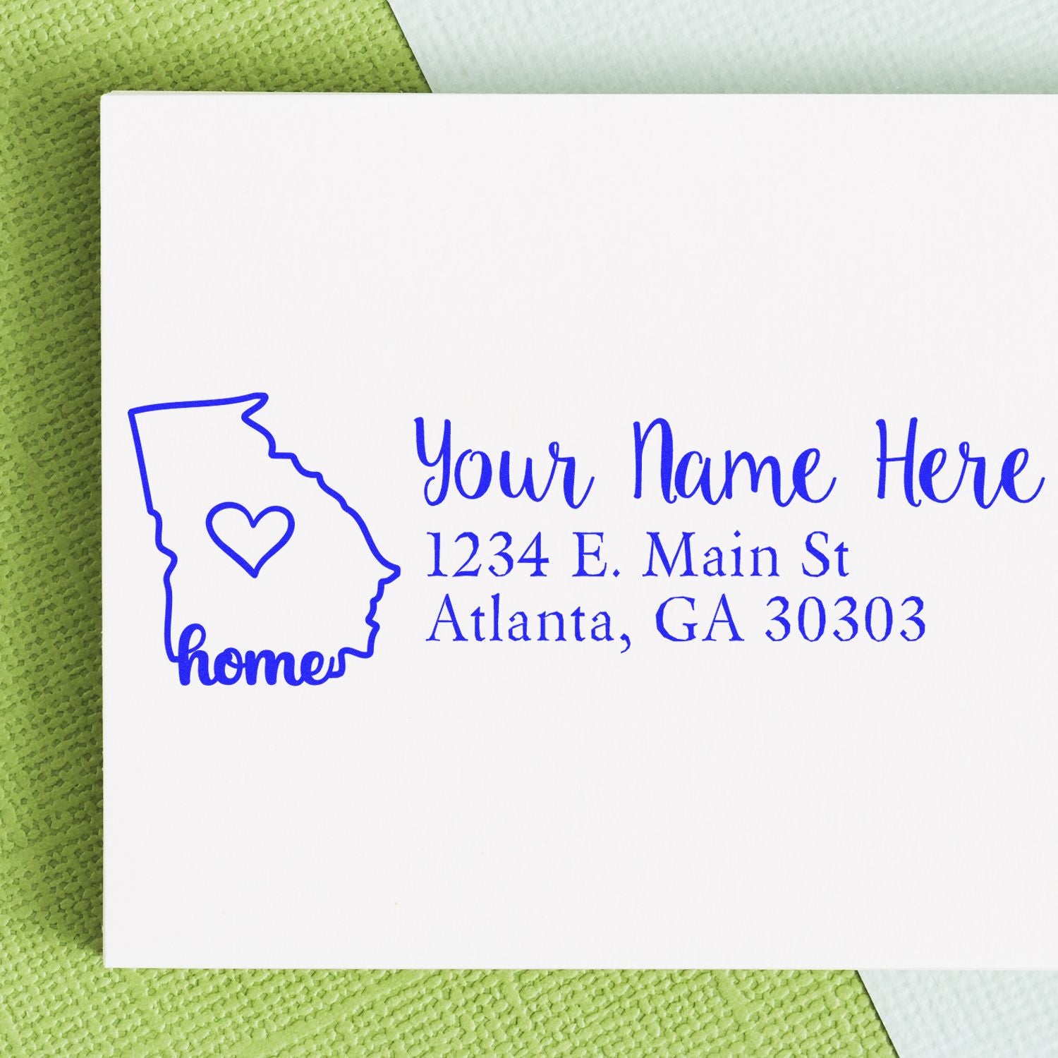 Georgia Self-Inking State Love Address Stamp on white envelope with blue ink, featuring a Georgia outline with a heart and the word home. Address reads: 1234 E. Main St, Atlanta, GA 30303.