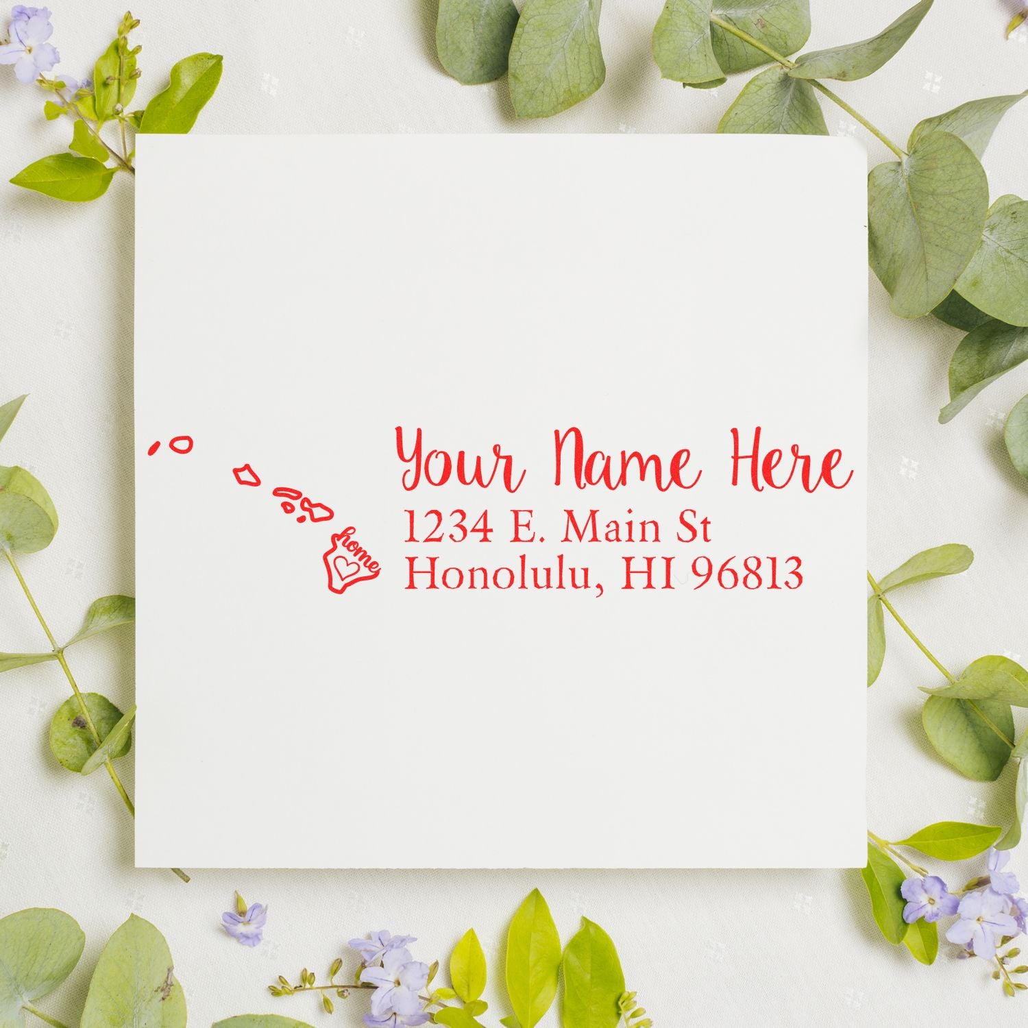 Slim Pre-Inked Hawaii State Love Custom Address Stamp on white paper with red ink, featuring a heart and island design. Surrounded by green leaves and small purple flowers for a decorative touch.