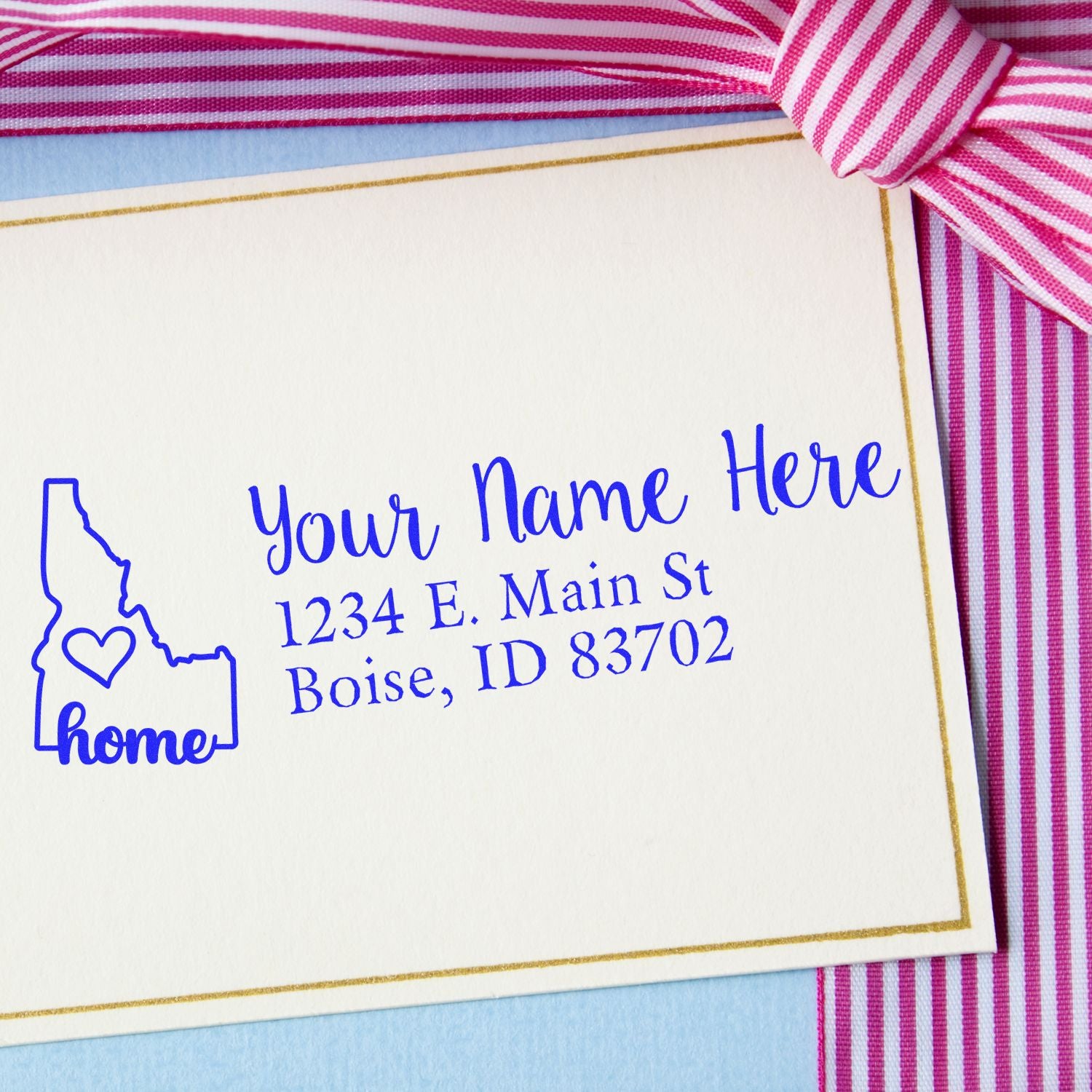 PSI Pre-Inked Personalized Idaho State Love Address Stamp on a card with a pink striped ribbon, featuring a heart inside the Idaho outline and sample text: Your Name Here, 1234 E. Main St, Boise, ID 83702.