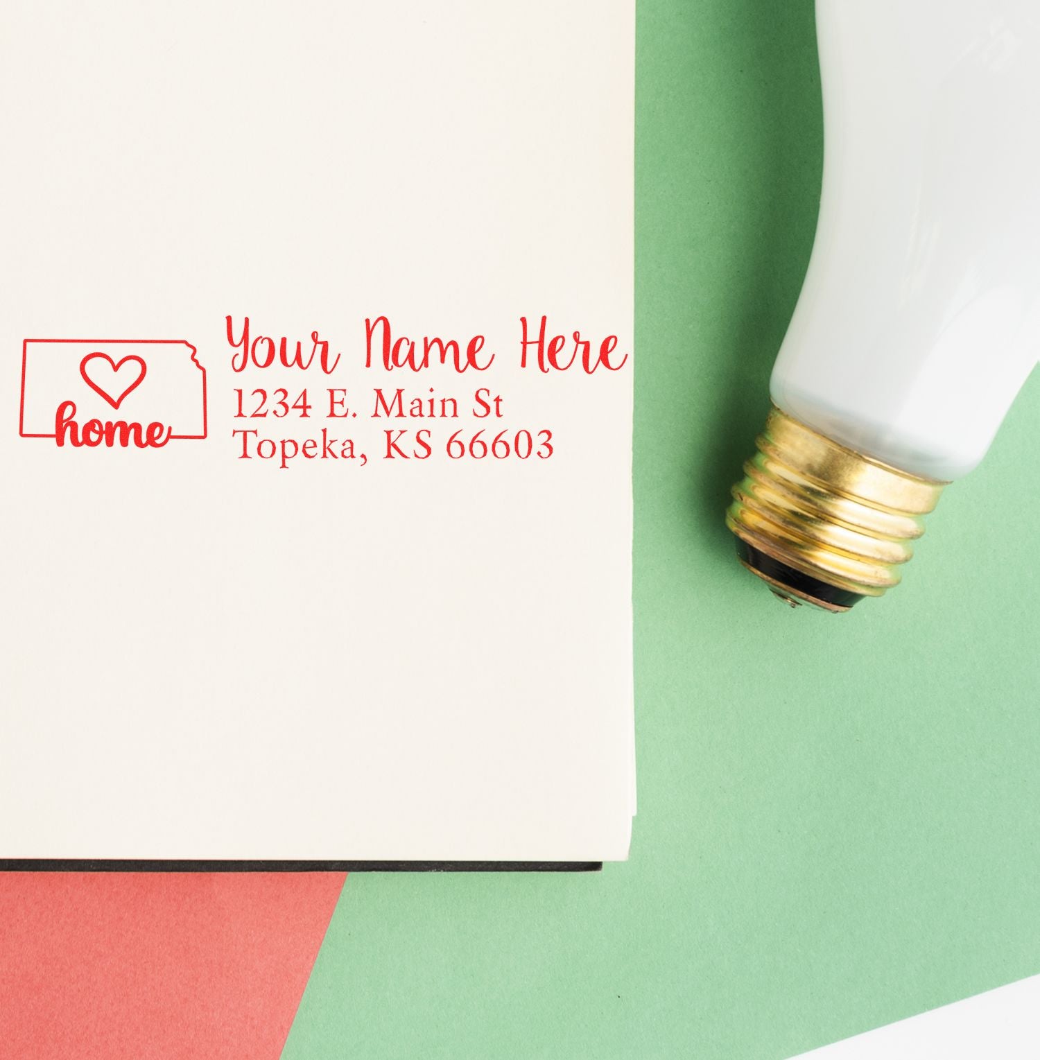 PSI Pre-Inked Personalized Kansas State Love Address Stamp on an envelope, featuring a red heart design and customizable address, placed on a colorful background with a light bulb nearby.