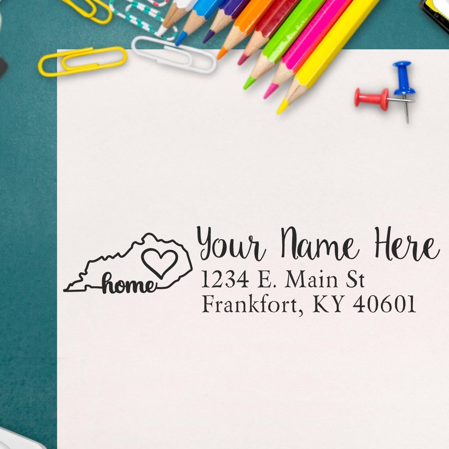 Kentucky Self-Inking State Love Address Stamp on paper with colorful pencils and paperclips. Features a heart design and customizable address for Frankfort, KY.