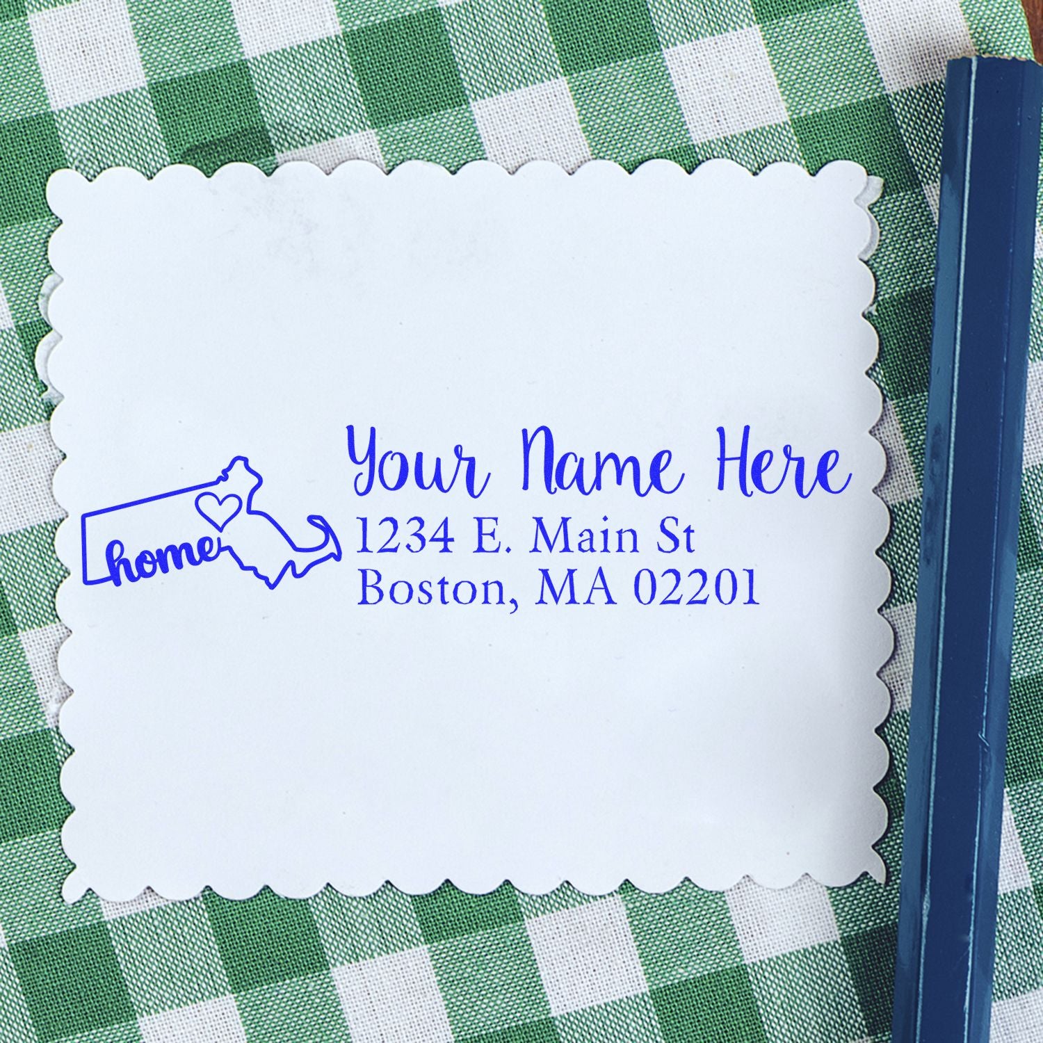 Wood Handle Massachusetts Custom Address Rubber Stamp on a scalloped card with a blue ink design, featuring a map outline and heart, placed on a green checkered tablecloth next to a blue pen.