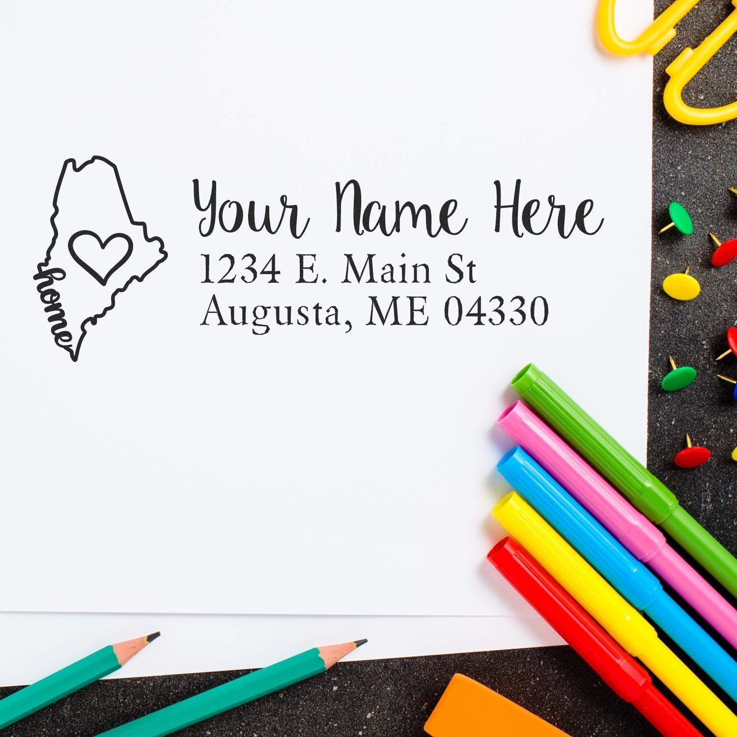 Maine Self-Inking State Love Address Stamp on white paper with colorful pens and push pins. Features a heart design within the state outline, perfect for personalizing mail with a touch of home.