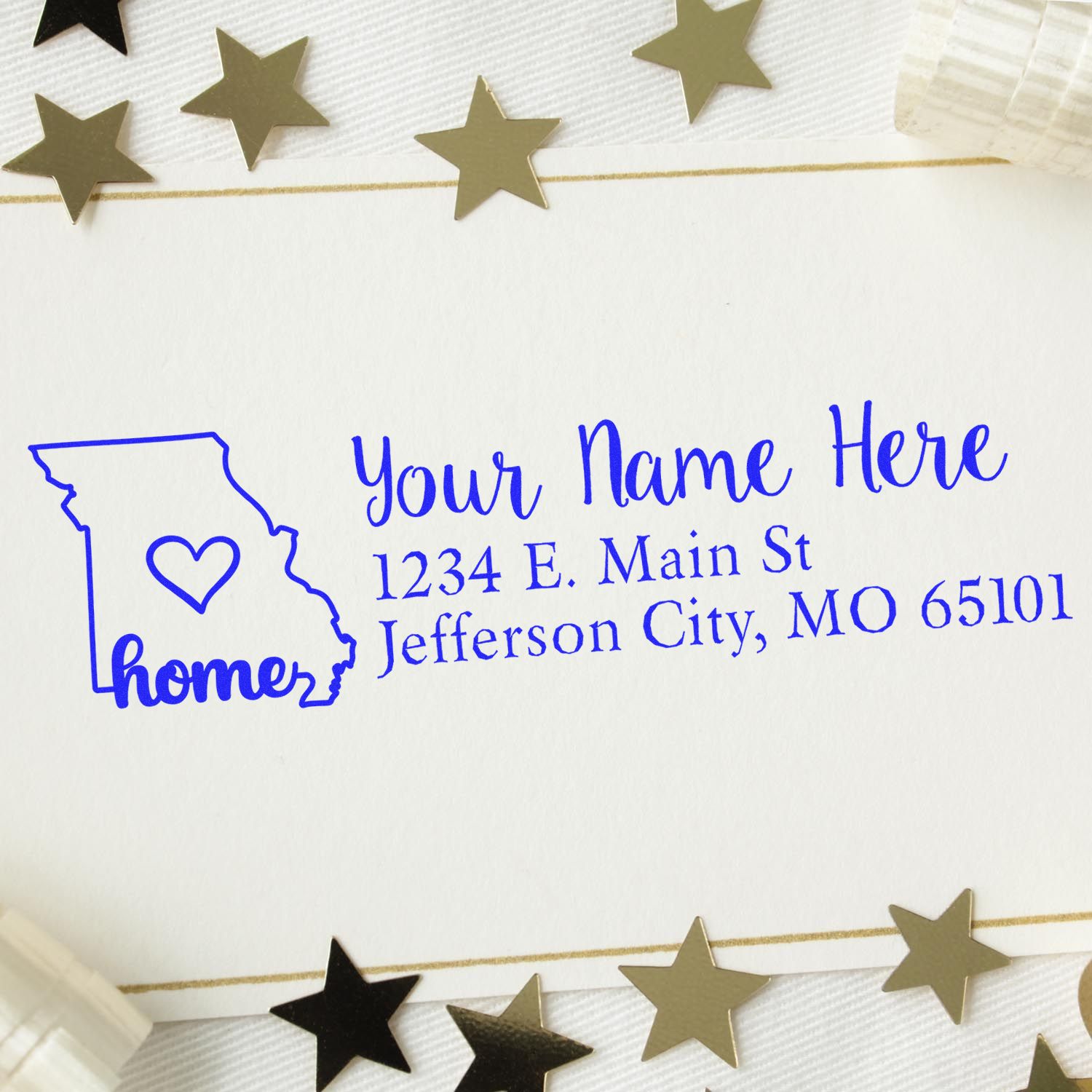 Slim Pre-Inked Missouri State Love Custom Address Stamp on white paper, featuring a blue outline of Missouri with a heart and sample address. Surrounded by gold star decorations.