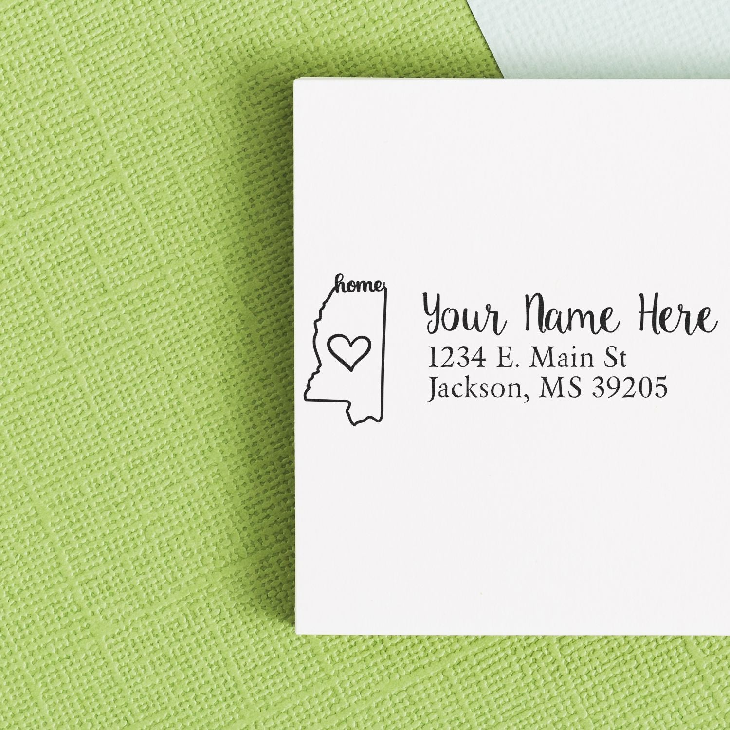 Mississippi Self-Inking State Love Address Stamp on a white envelope with a green textured background, featuring a heart inside the state outline and customizable address text.