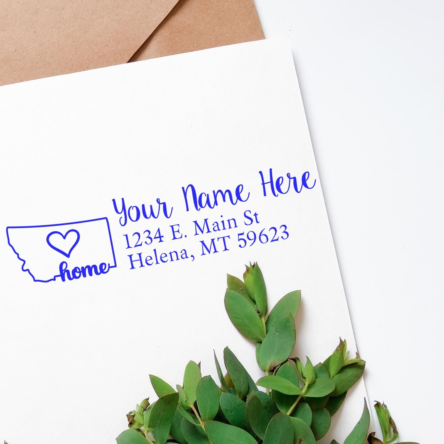 Montana Self-Inking State Love Address Stamp on white envelope with green leaves. Features a heart in Montana outline and customizable address text in blue.