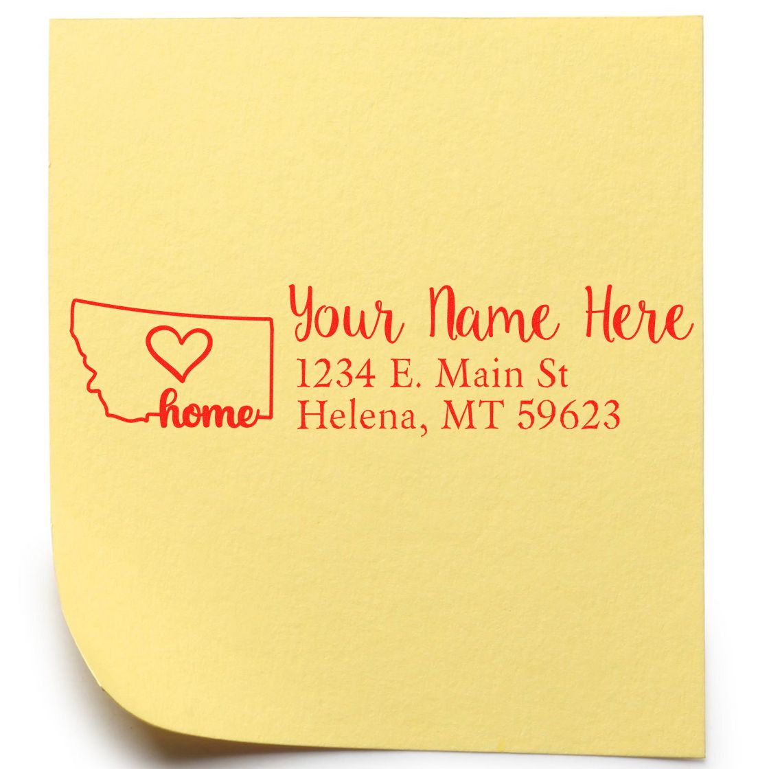 Yellow paper with red ink showing the Montana Self-Inking State Love Address Stamp design, featuring a heart inside the state outline and sample address text: Your Name Here, 1234 E. Main St, Helena, MT 59623.