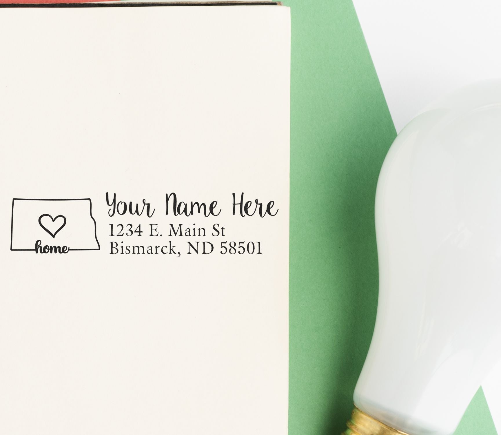 North Dakota Self-Inking State Love Address Stamp on an envelope with a heart design, next to a green paper and a light bulb.