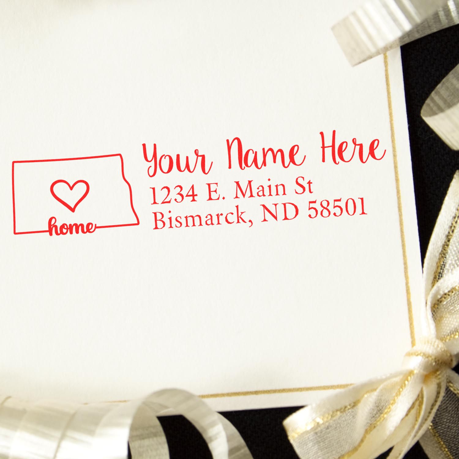 Wood Handle North Dakota Custom Address Rubber Stamp on a card with a heart design, featuring a sample address in red ink. The card is adorned with gold and silver ribbons.