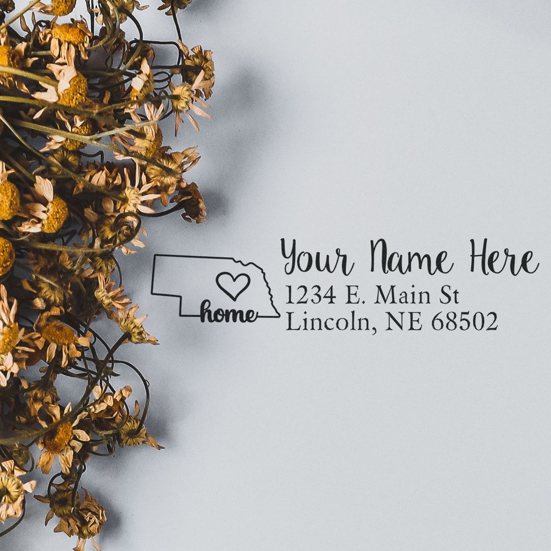 Nebraska Self-Inking State Love Address Stamp on paper with dried flowers, featuring a heart design and customizable address for a personal touch.