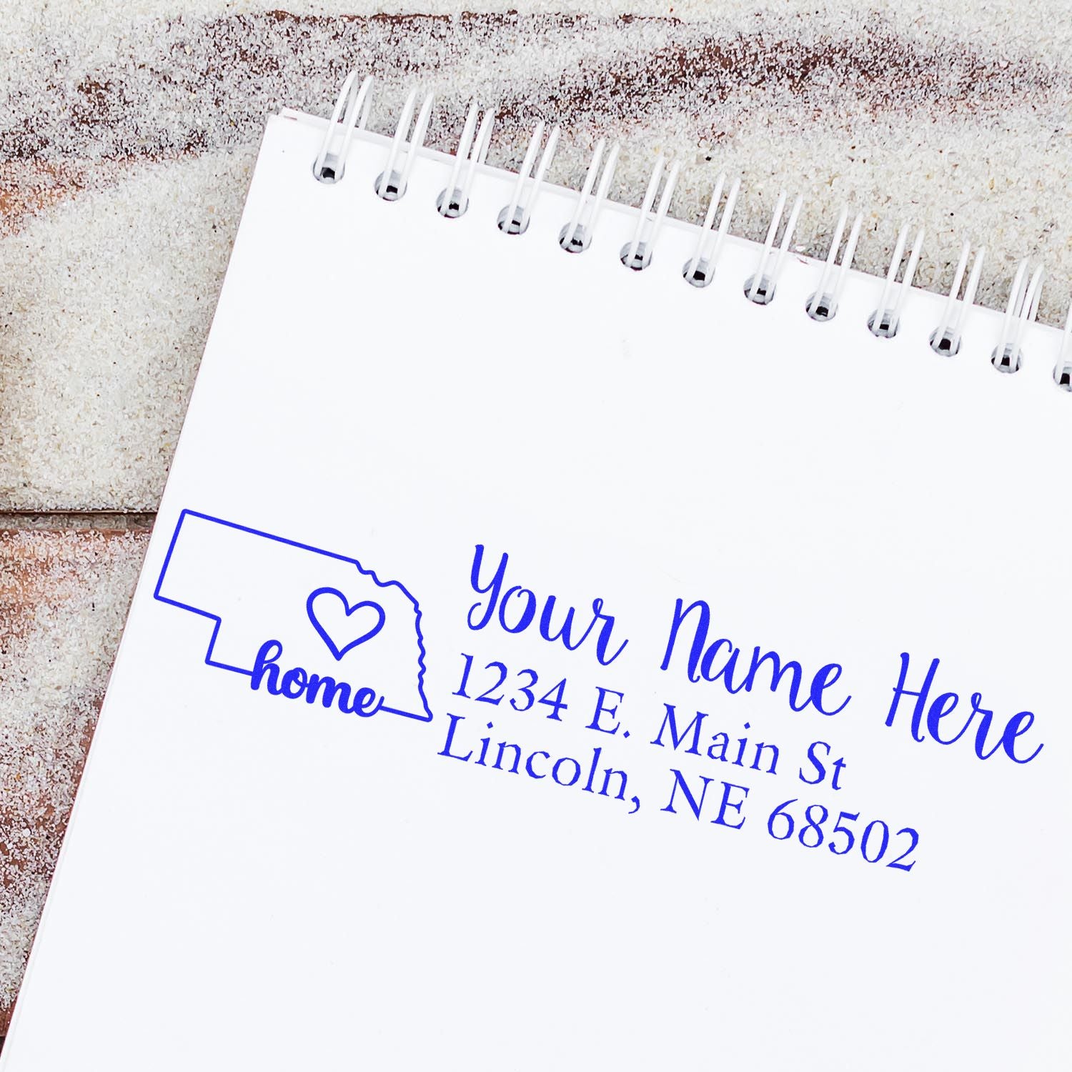 Wood Handle Nebraska Custom Address Rubber Stamp on a notepad, featuring a heart design and sample address in blue ink. Perfect for personalized mail and stationery.