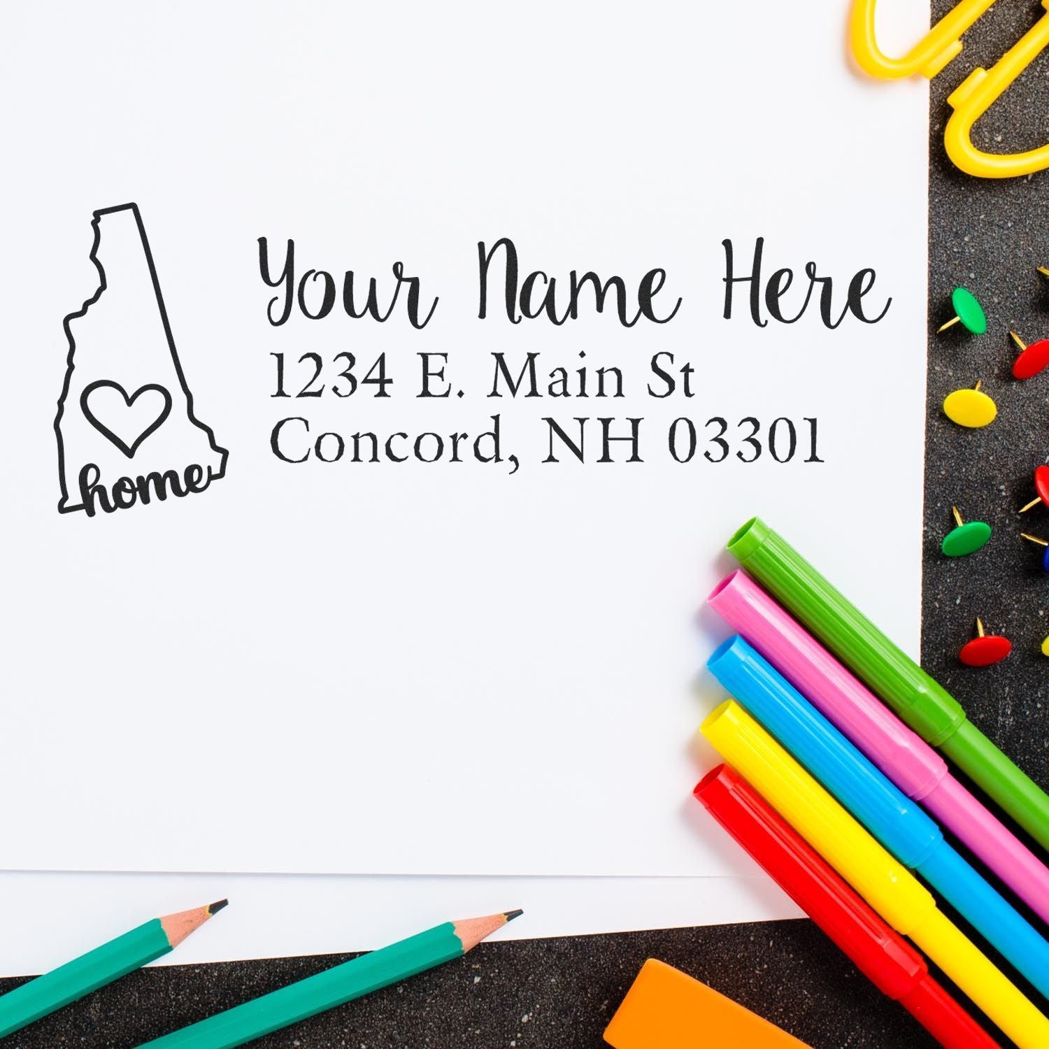 Wood Handle New Hampshire Custom Address Rubber Stamp on white paper with colorful pens and push pins. Features a state outline with home text, personalized address, and Concord, NH details.