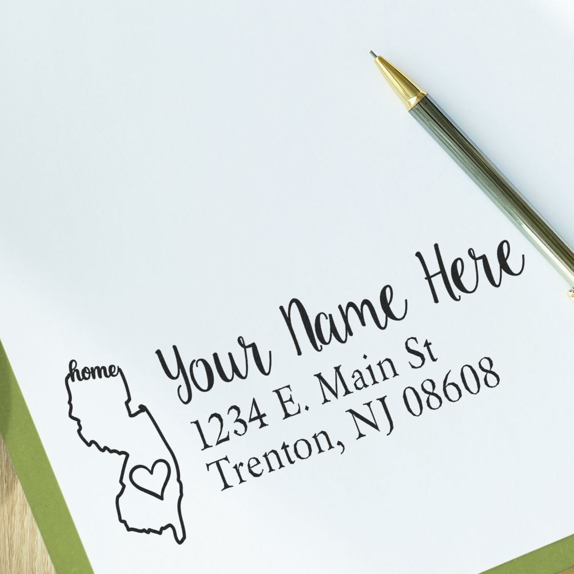 Wood Handle New Jersey Custom Address Rubber Stamp on white paper, featuring a heart design within the state outline and personalized address text. Pen nearby on a green folder.