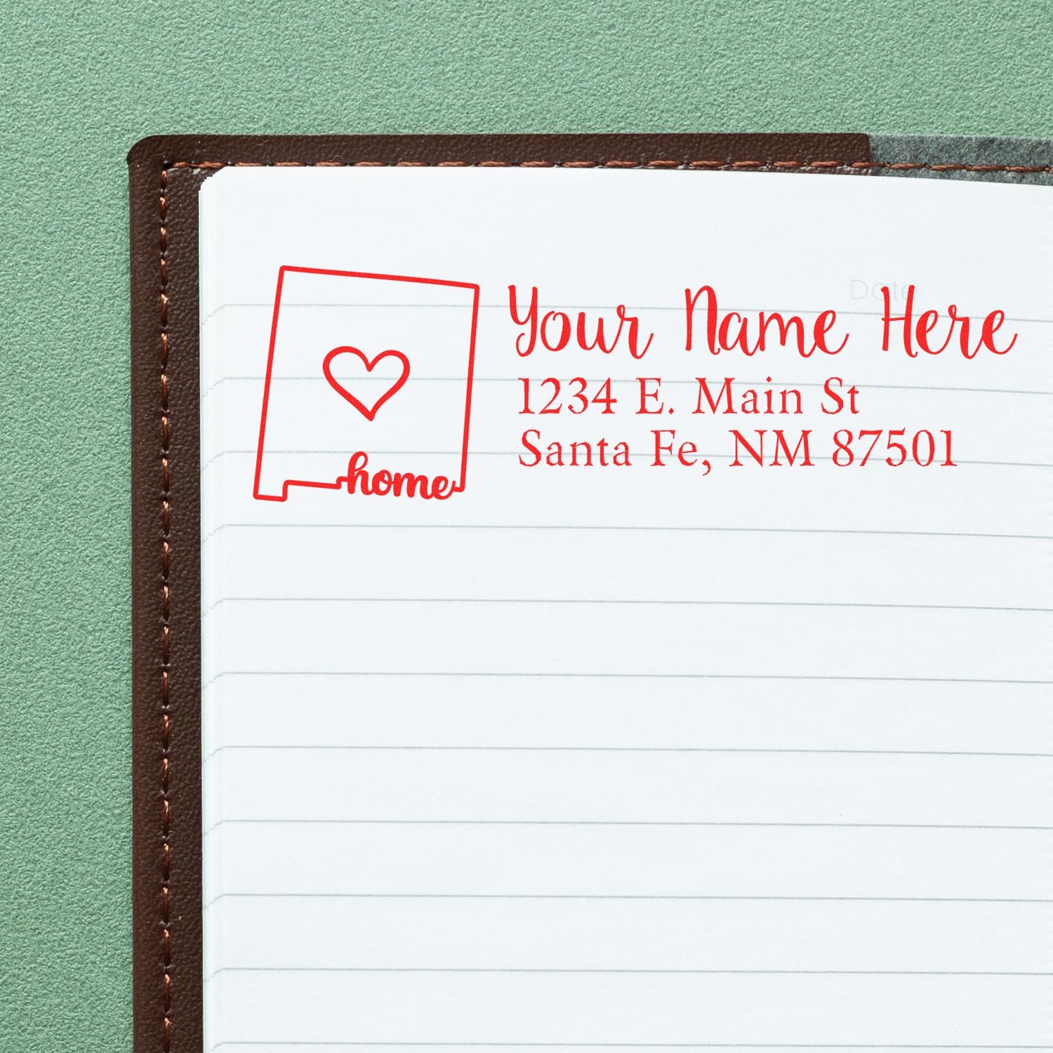 New Mexico Self-Inking State Love Address Stamp on a notebook page, featuring a red outline of New Mexico with a heart and the word home, alongside customizable address text.